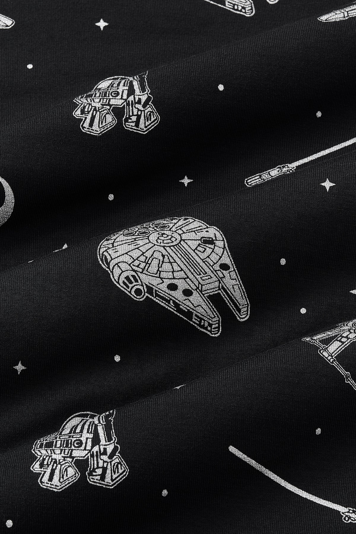 Close up of bamboo fabric: A repeating, monochromatic print featuring: a grey Milennium Falcon; a grey X-wing starfighter; a grey R2-D2; a grey lightsaber; a grey Rebel Alliance starbird symbol; and various grey twinkles and dots, over a black background.