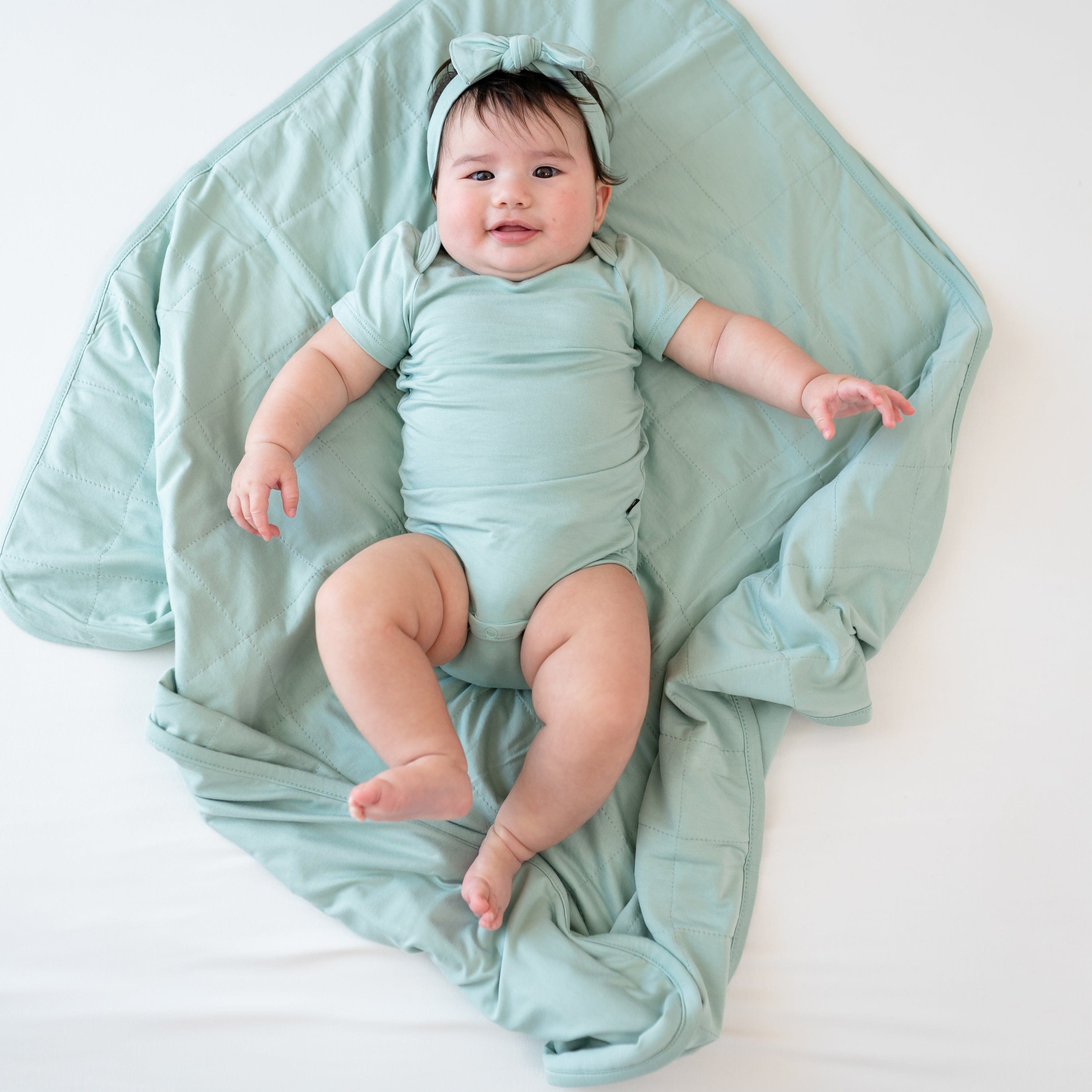 Baby in Sage bodysuit laying on Baby Blanket in Sage 1.0