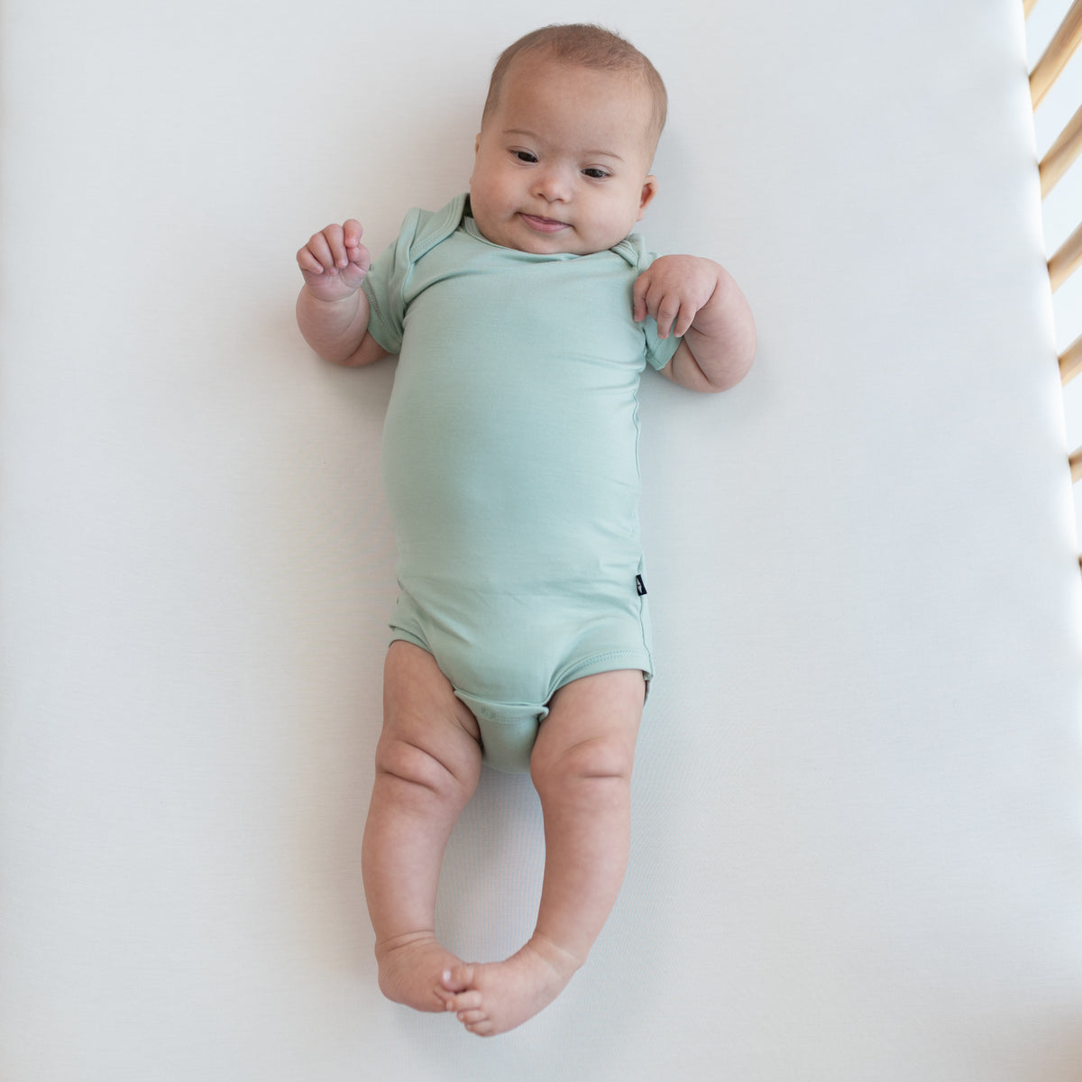 Baby wearing Bodysuit in Sage in a crib