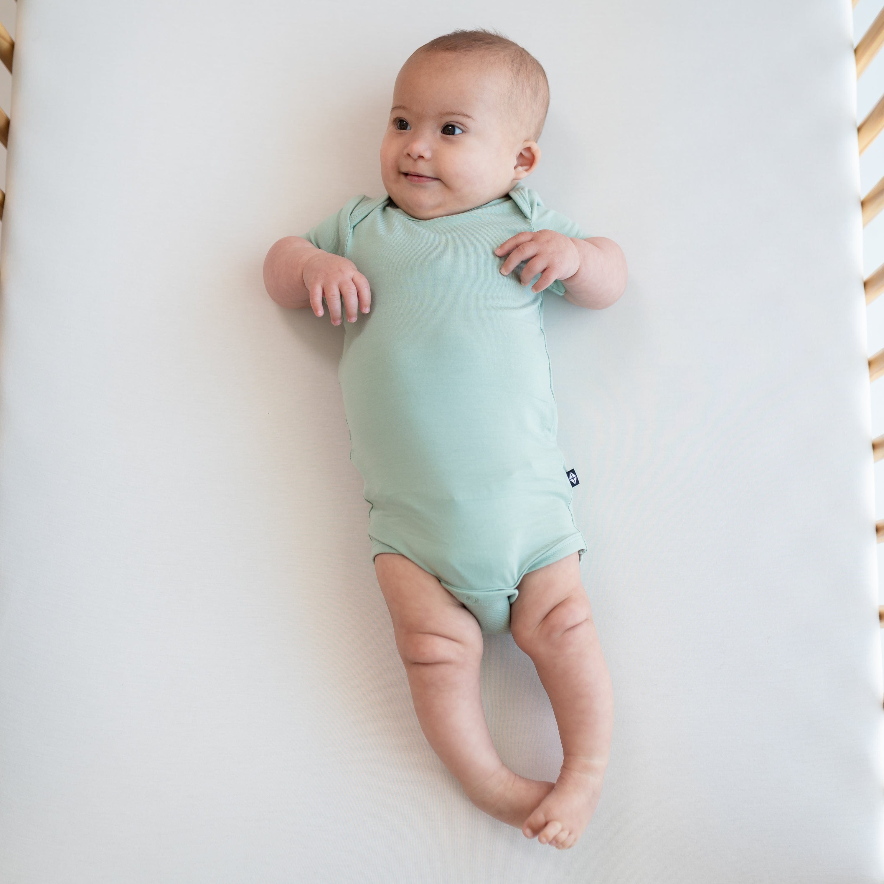 Baby wearing Bodysuit in Sage in a crib
