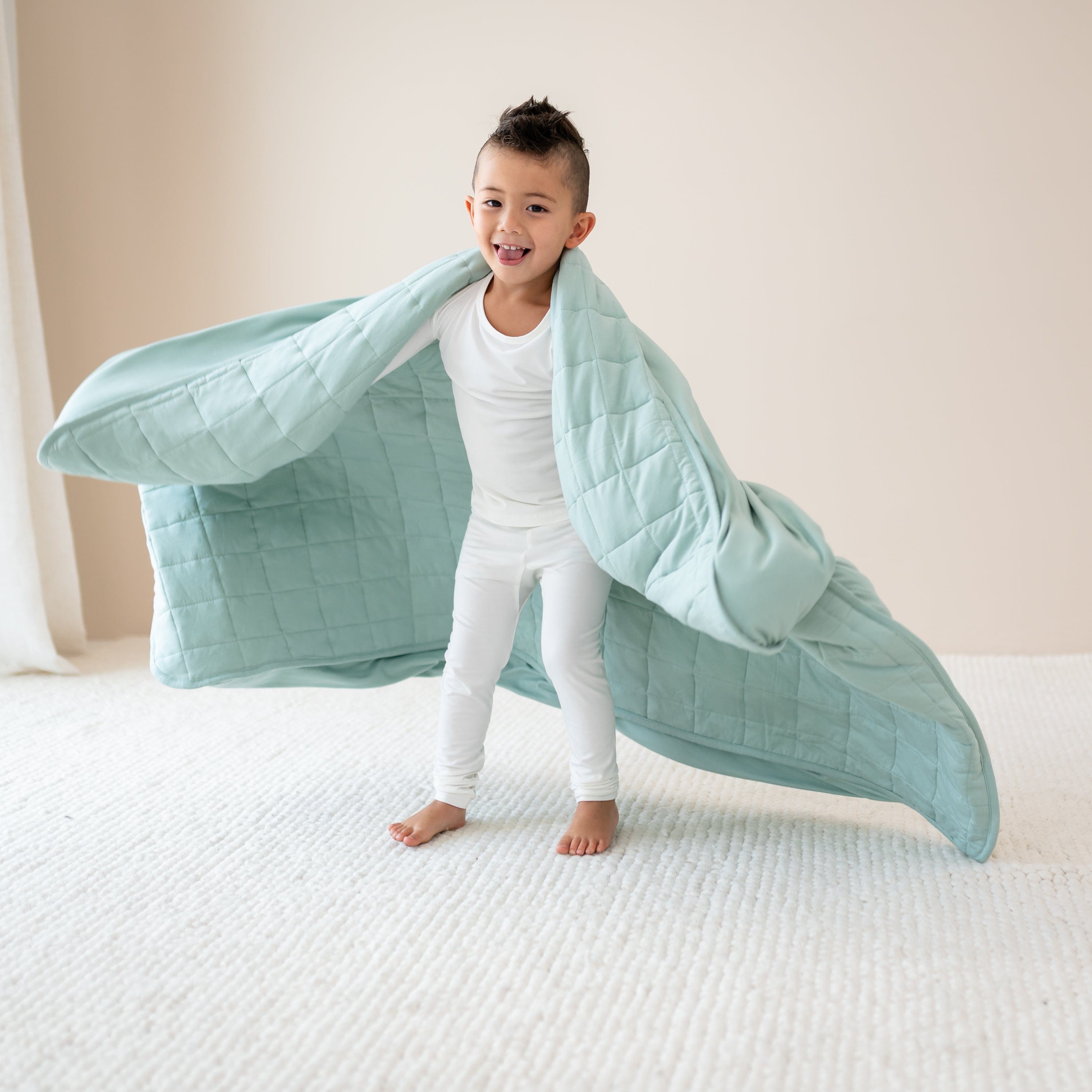 Child in Cloud Pajamas playing spinning with Youth Blanket in Sage 1.0