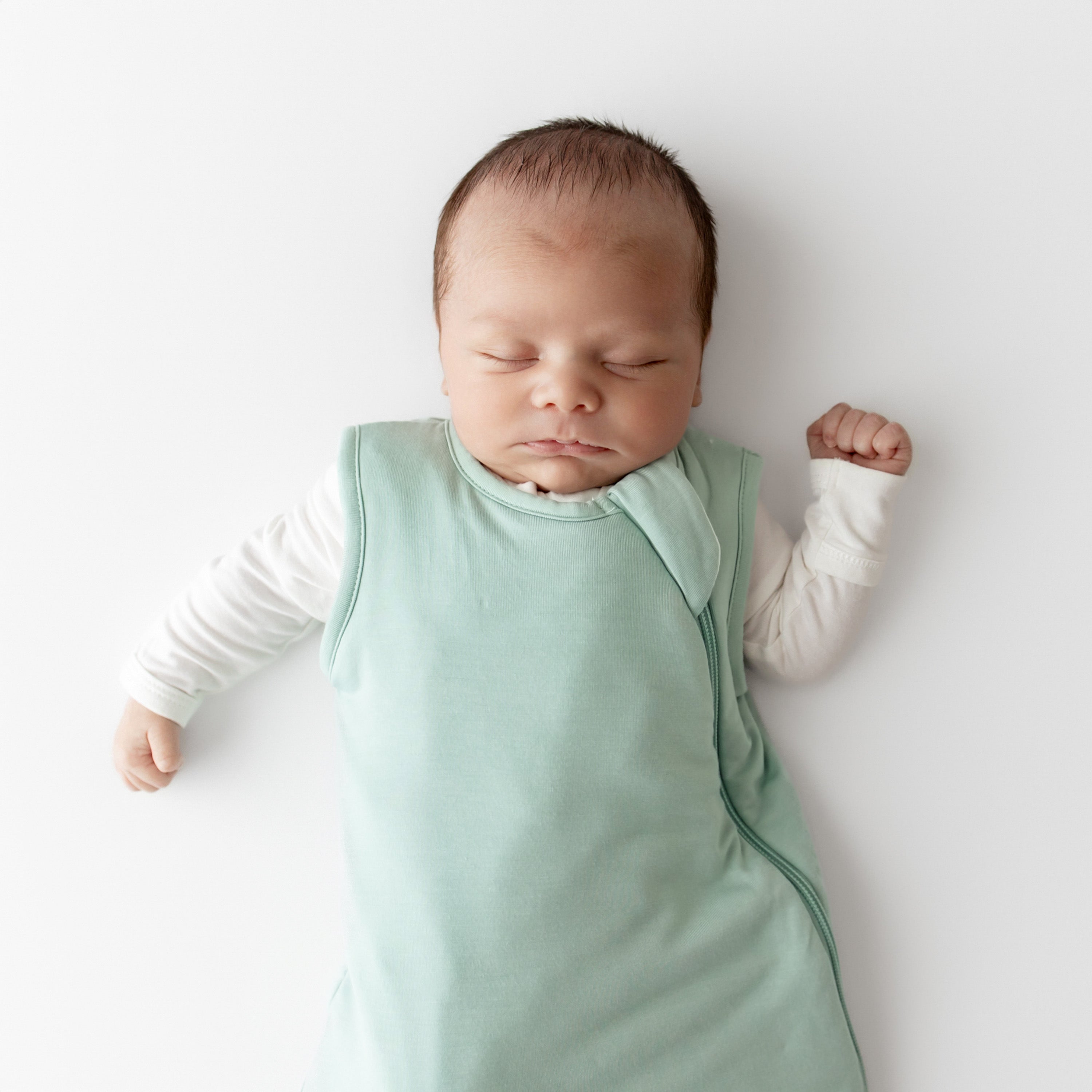 Newborn baby sleeping in a light green kyte baby sleep bag on a white background