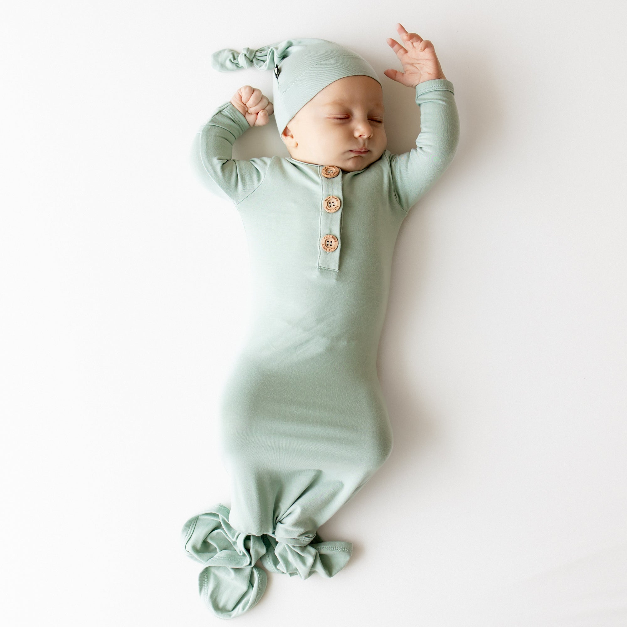 Baby asleep wearing kyte baby knotted gown and hat set in a sage green