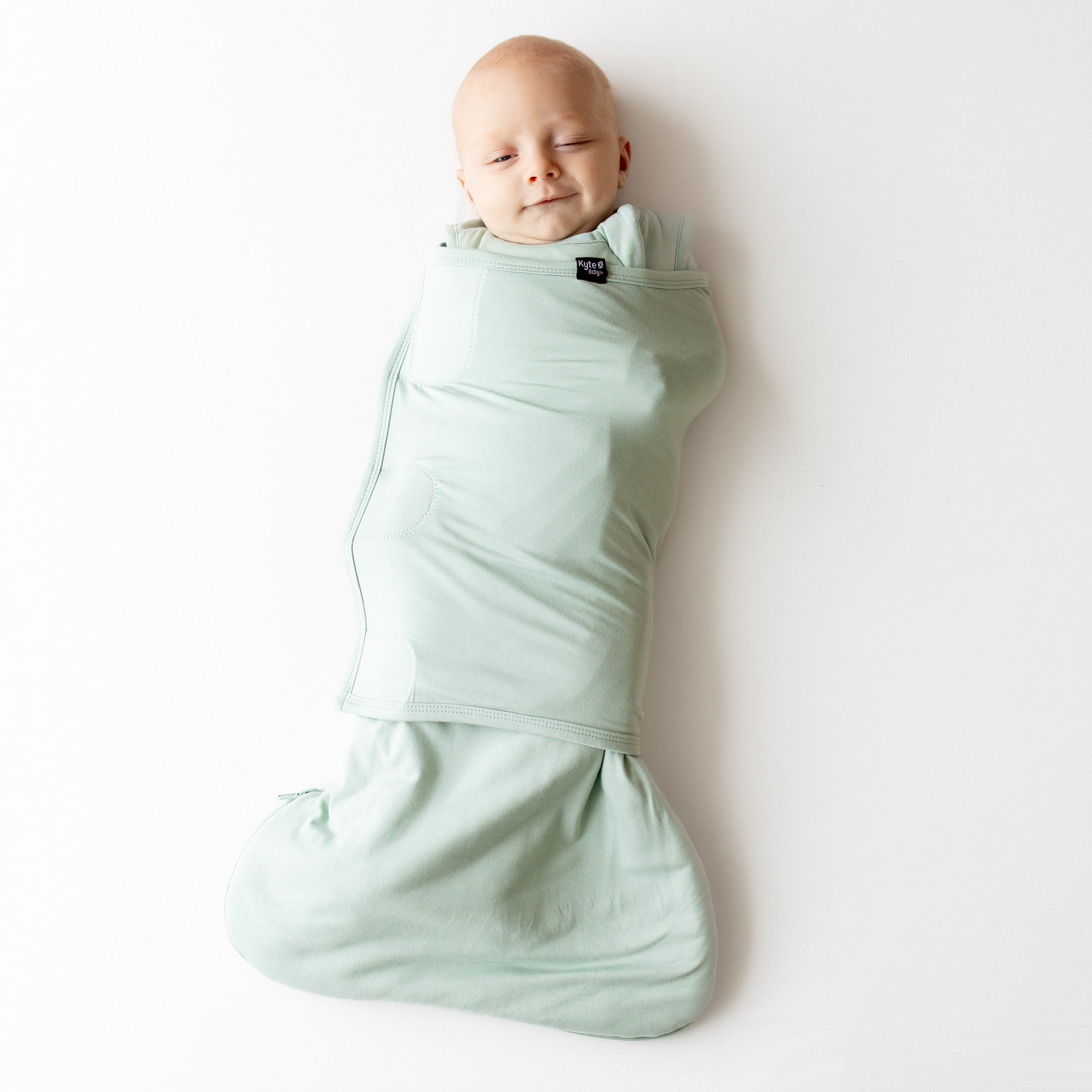 Baby swaddled in a light green swaddler on a white background