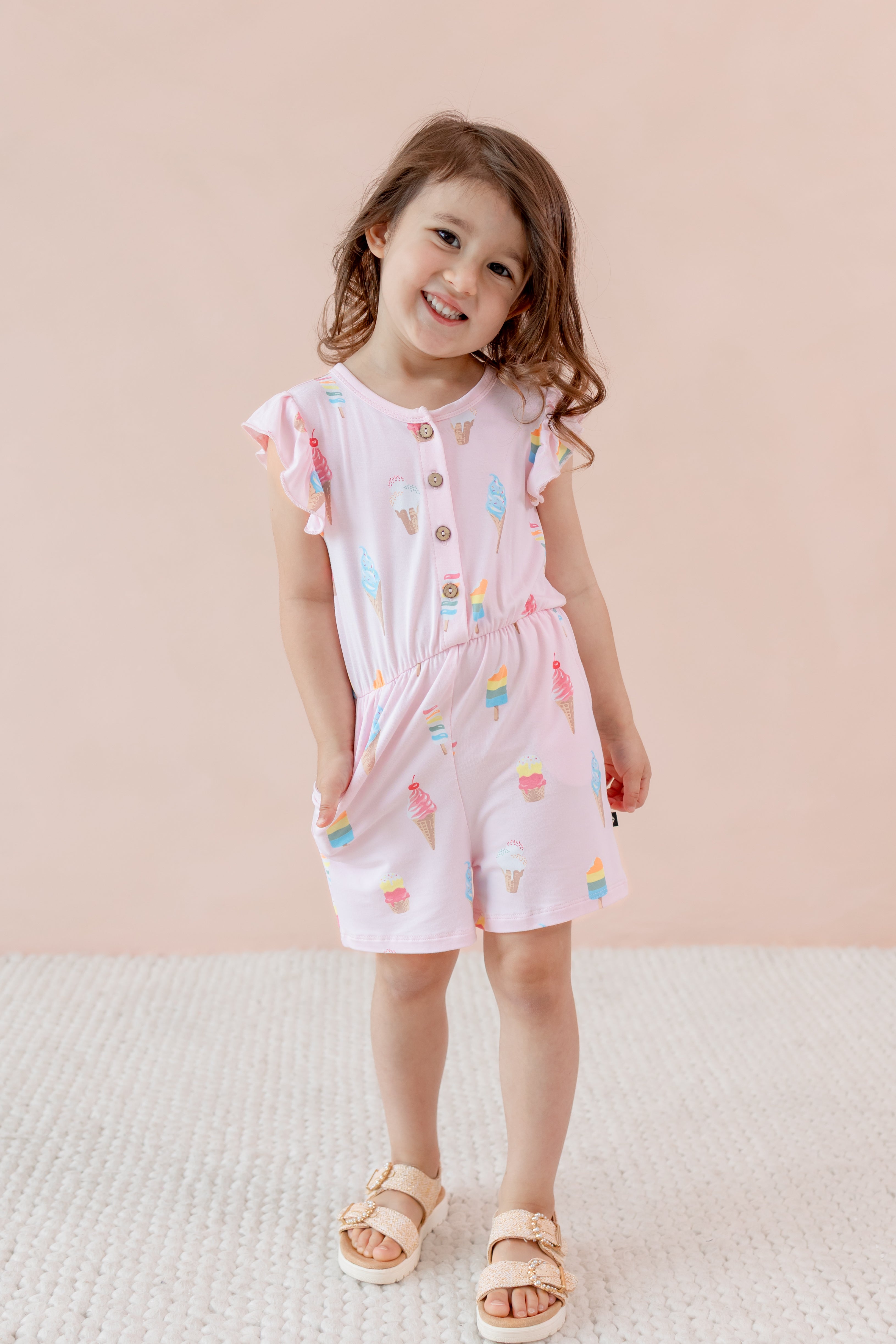 Child wearing in Sakura Ice cream print Flutter Sleeve Romper on a beige background with sandles