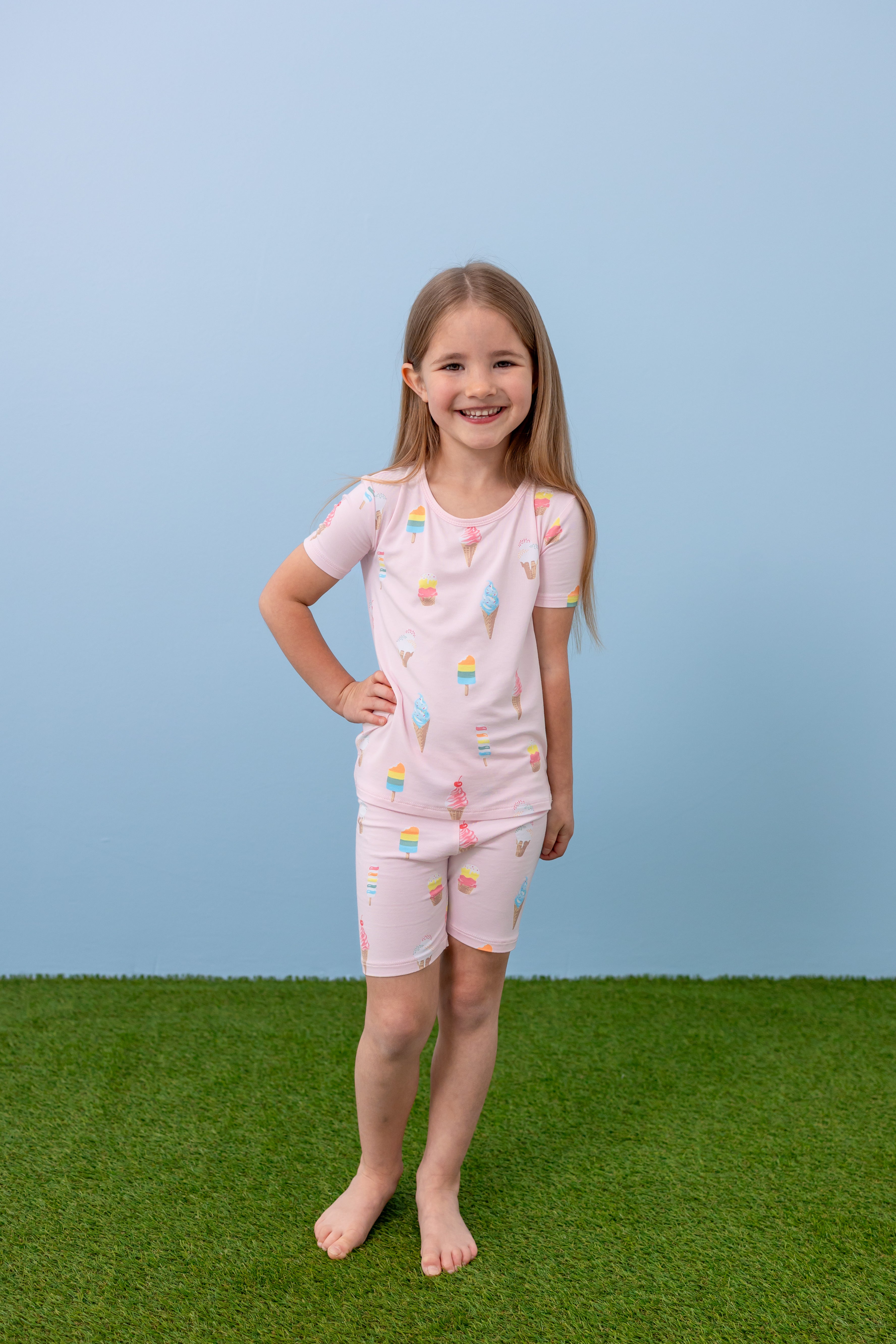 Child standing in Sakura Ice Cream print short sleeve pajama set on blue background and green grass