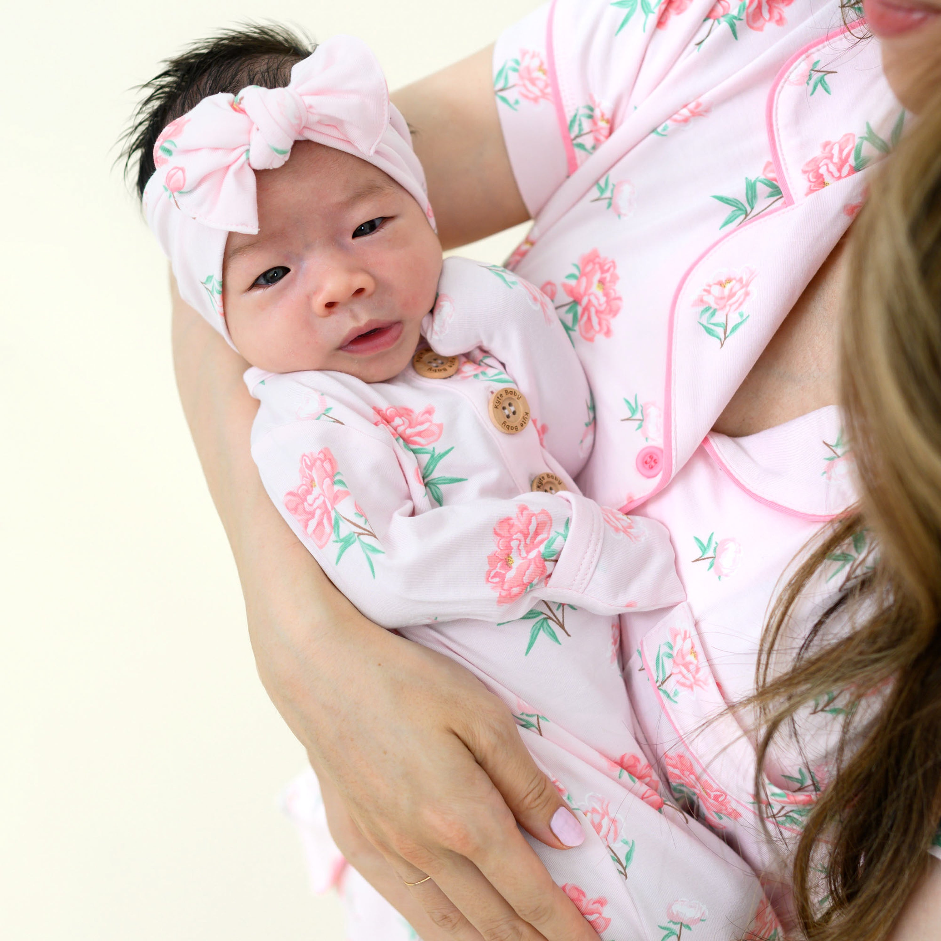 Close up of baby in Knotted Gown with Bow Set in Sakura Peony being held by mom