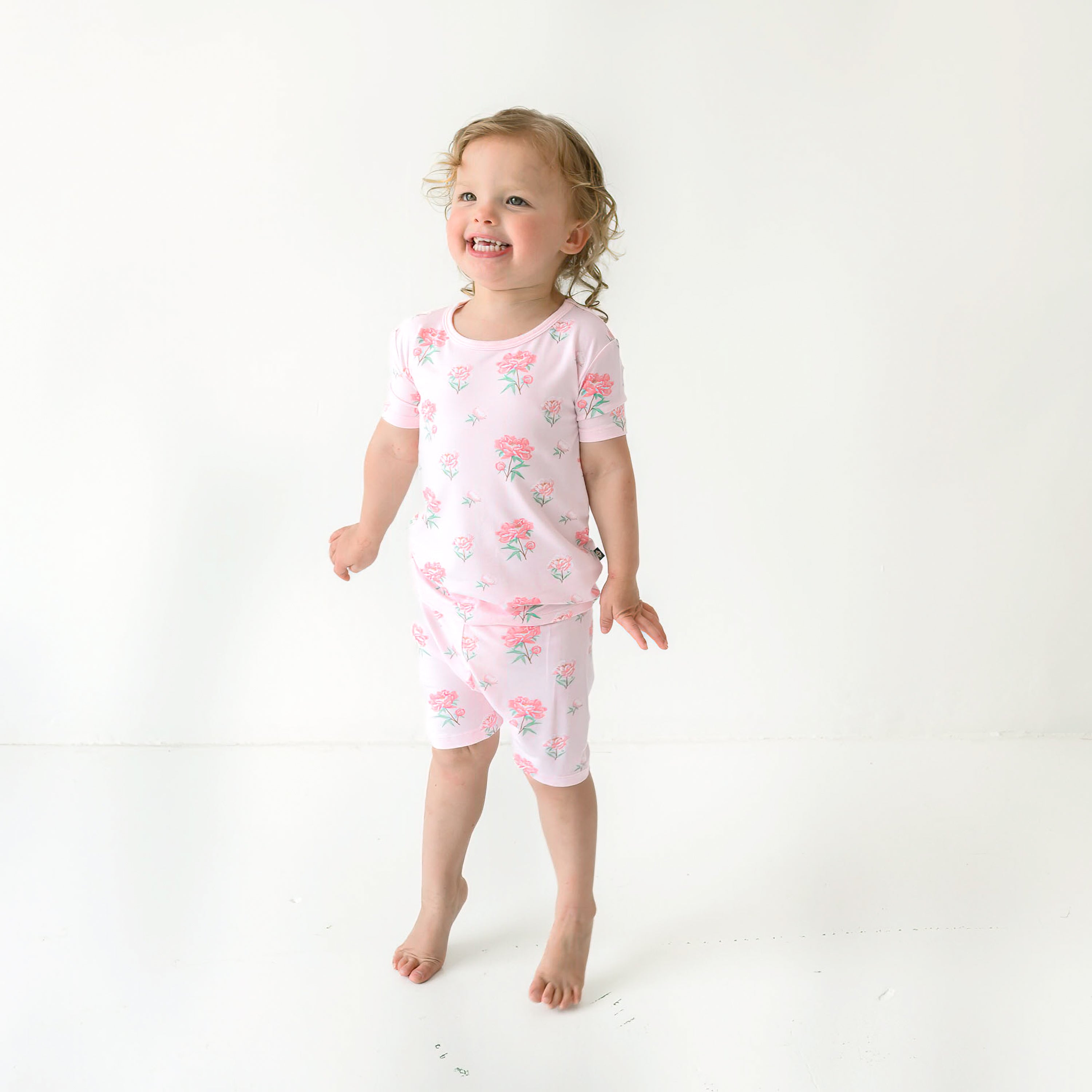 Smiling toddler standing on her tip toes wearing the Short Sleeve Pajamas in Sakura Peony