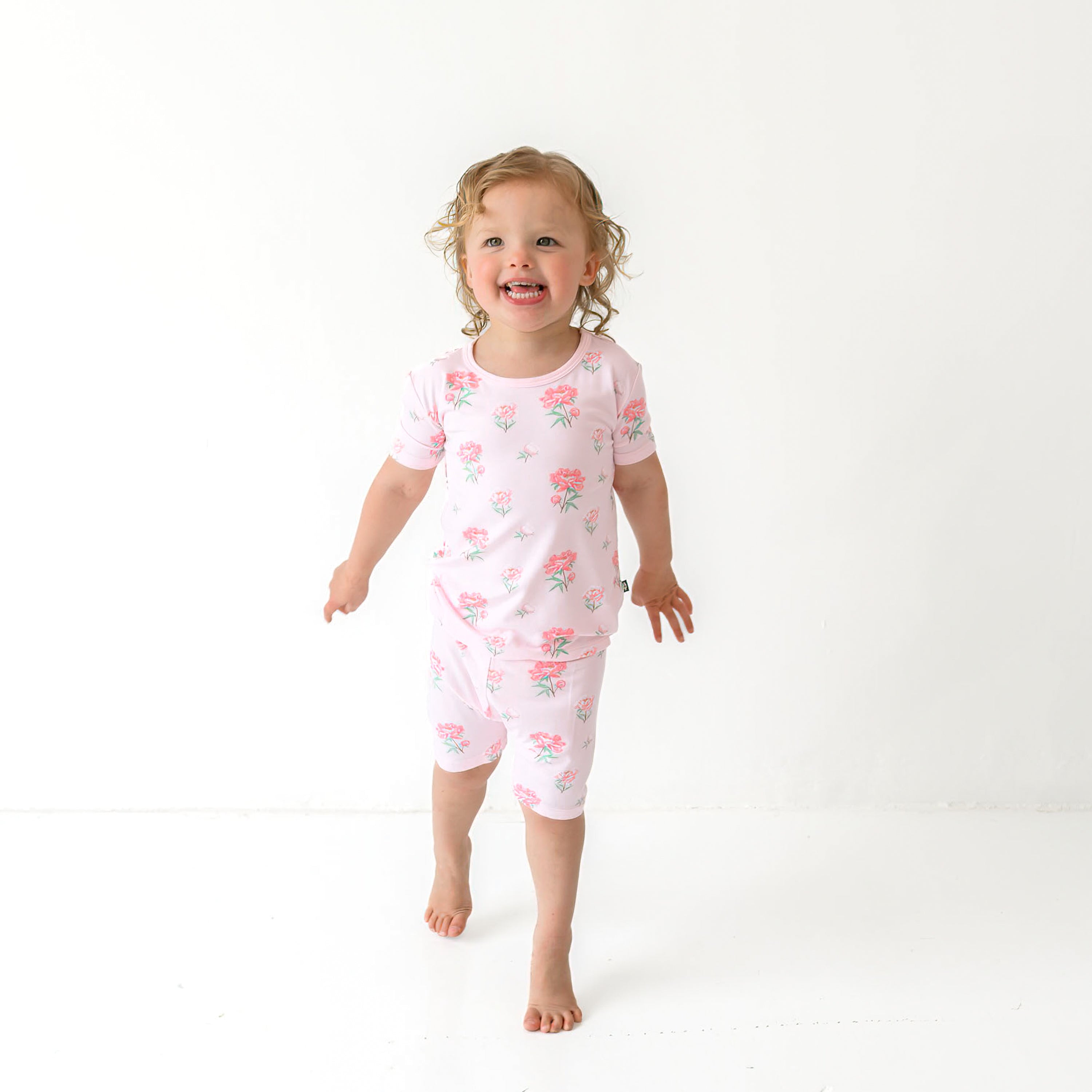 Toddler model walking wearing the Short Sleeve Pajamas in Sakura Peony