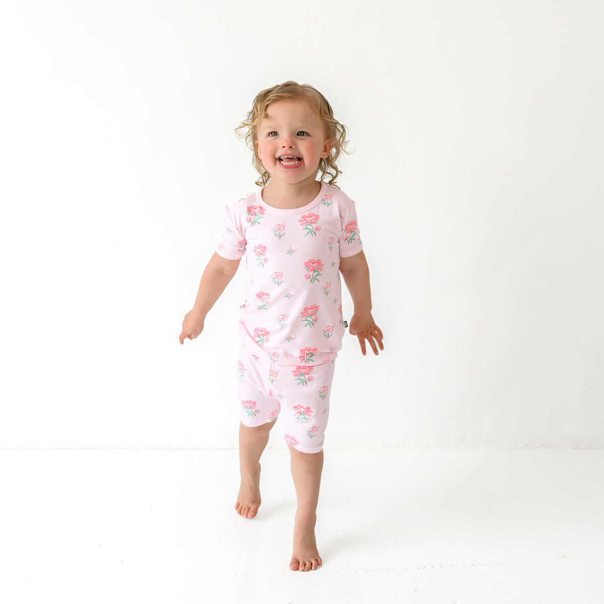 Toddler model walking wearing the Short Sleeve Pajamas in Sakura Peony