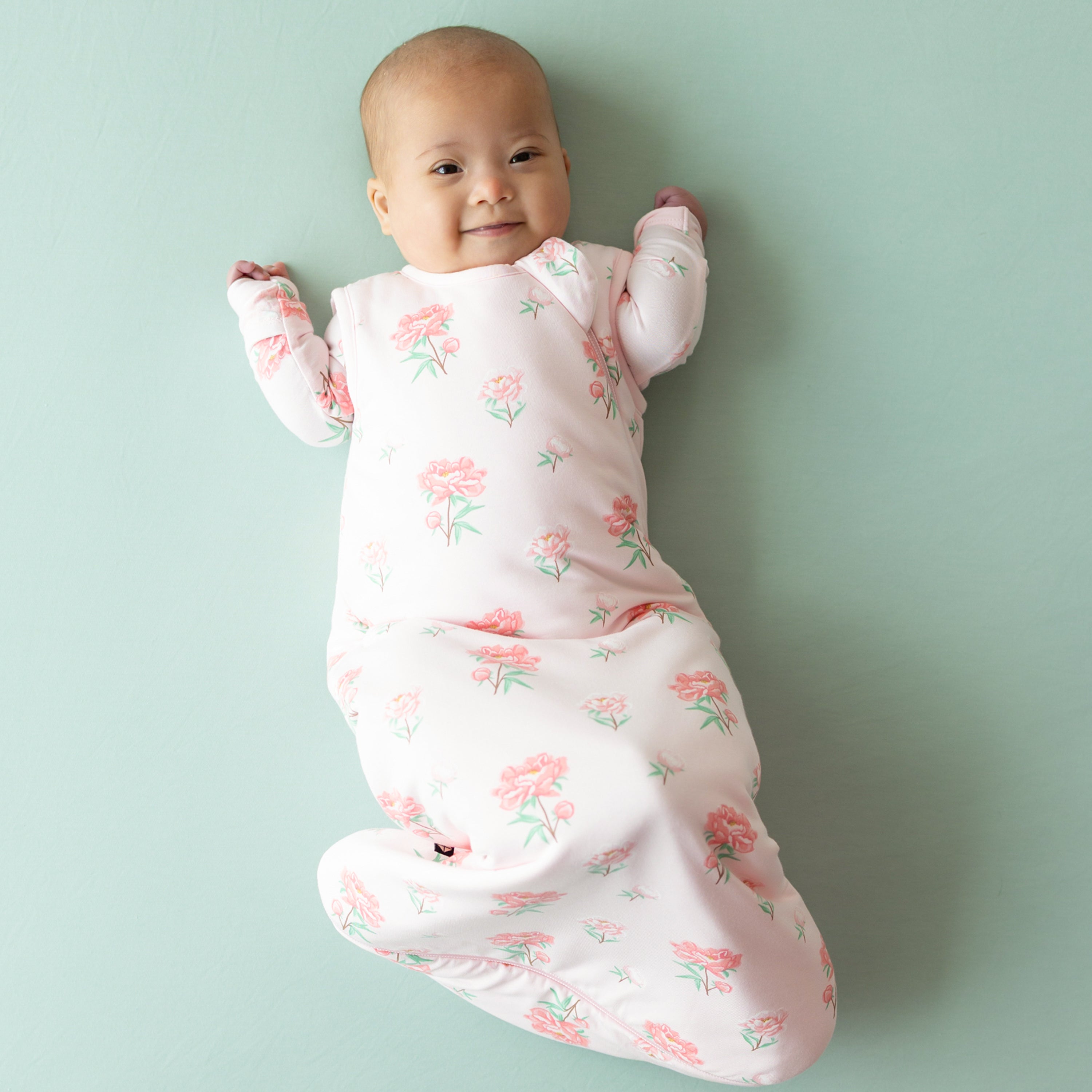 Smiling infant model wearing the Sleep Bag in Sakura Peony with the matching long sleeve romper on underneath