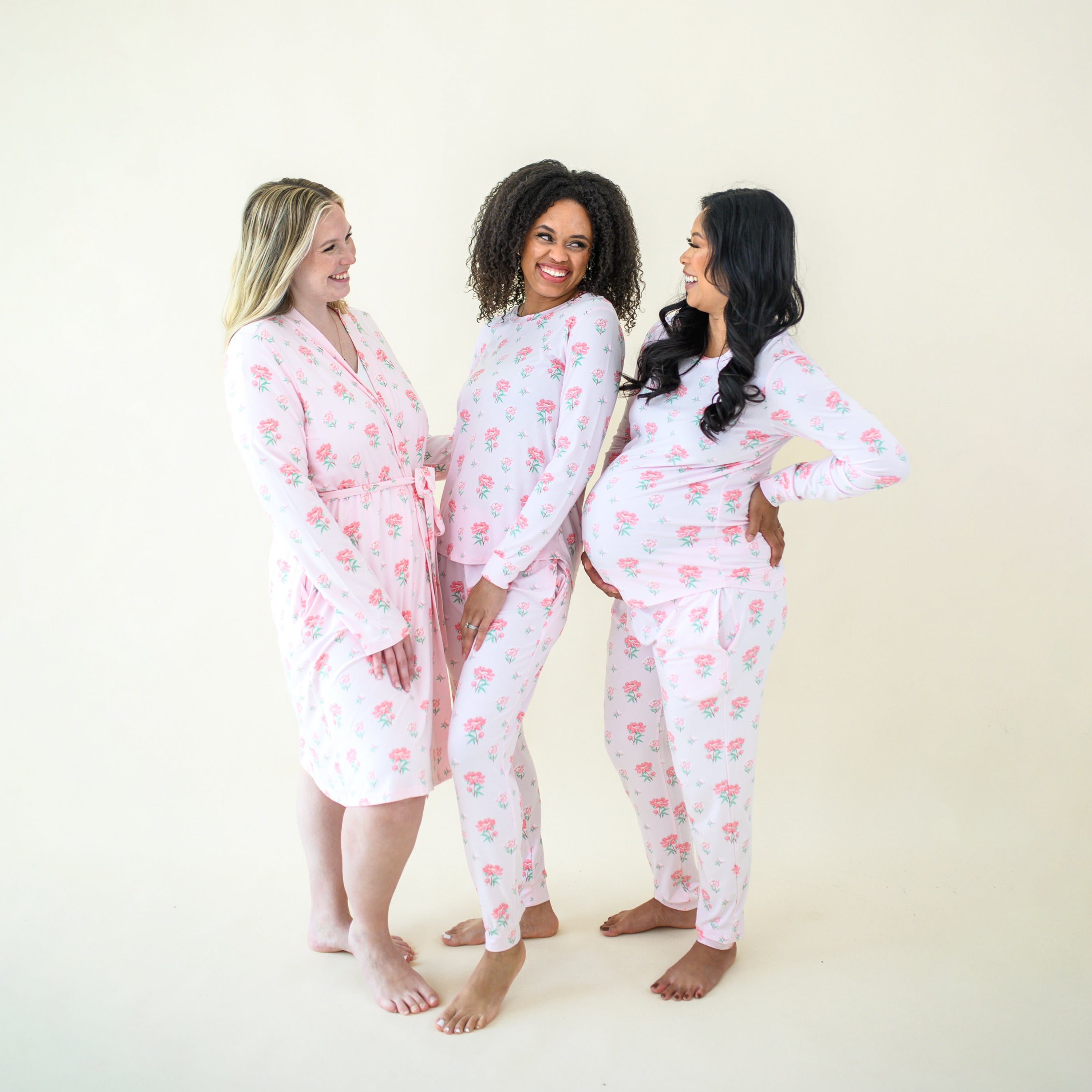 Three female models looking at one another smiling wearing items from the Sakura Peony Collection. Model one is wearing the Women's Lounge Robe, with the other two models wearing the Women's Jogger sets