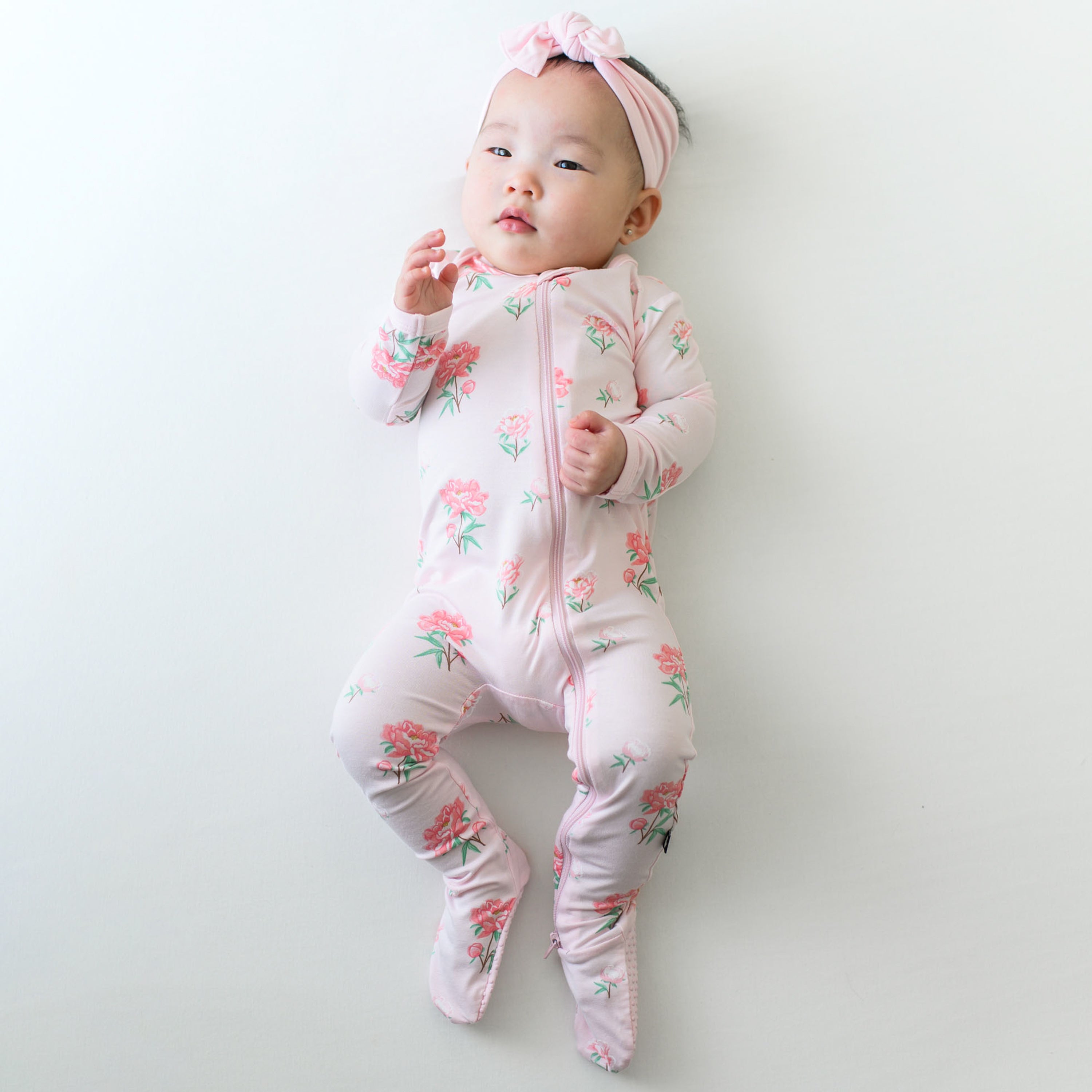 Infant wearing Zippered Footie in Sakura Peony with pink Knotted Bow Headband