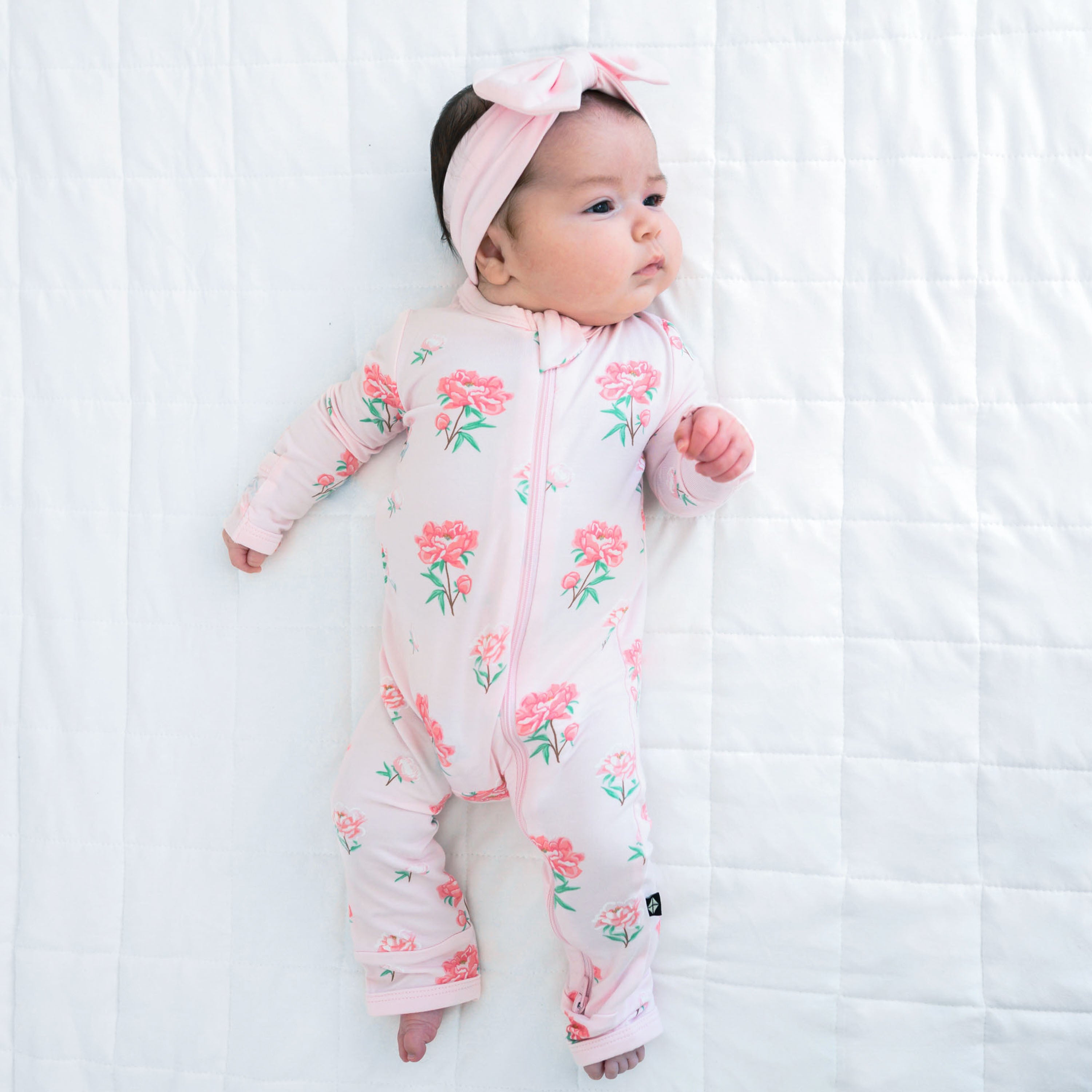 Newborn laying on a Cloud blanket wearing the Zippered Romper in Sakura Peony with Bow Headband in Sakura