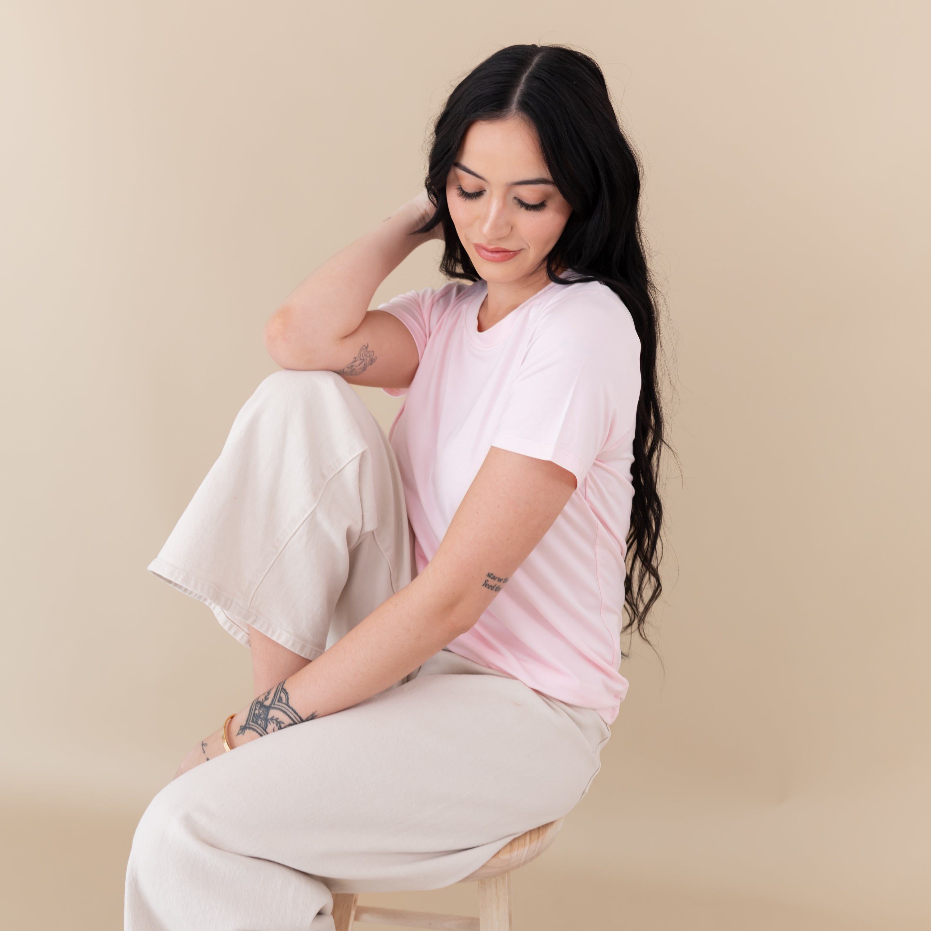 Woman modeling Women's Crew Neck Tee in Sakura sitting on stool looking down