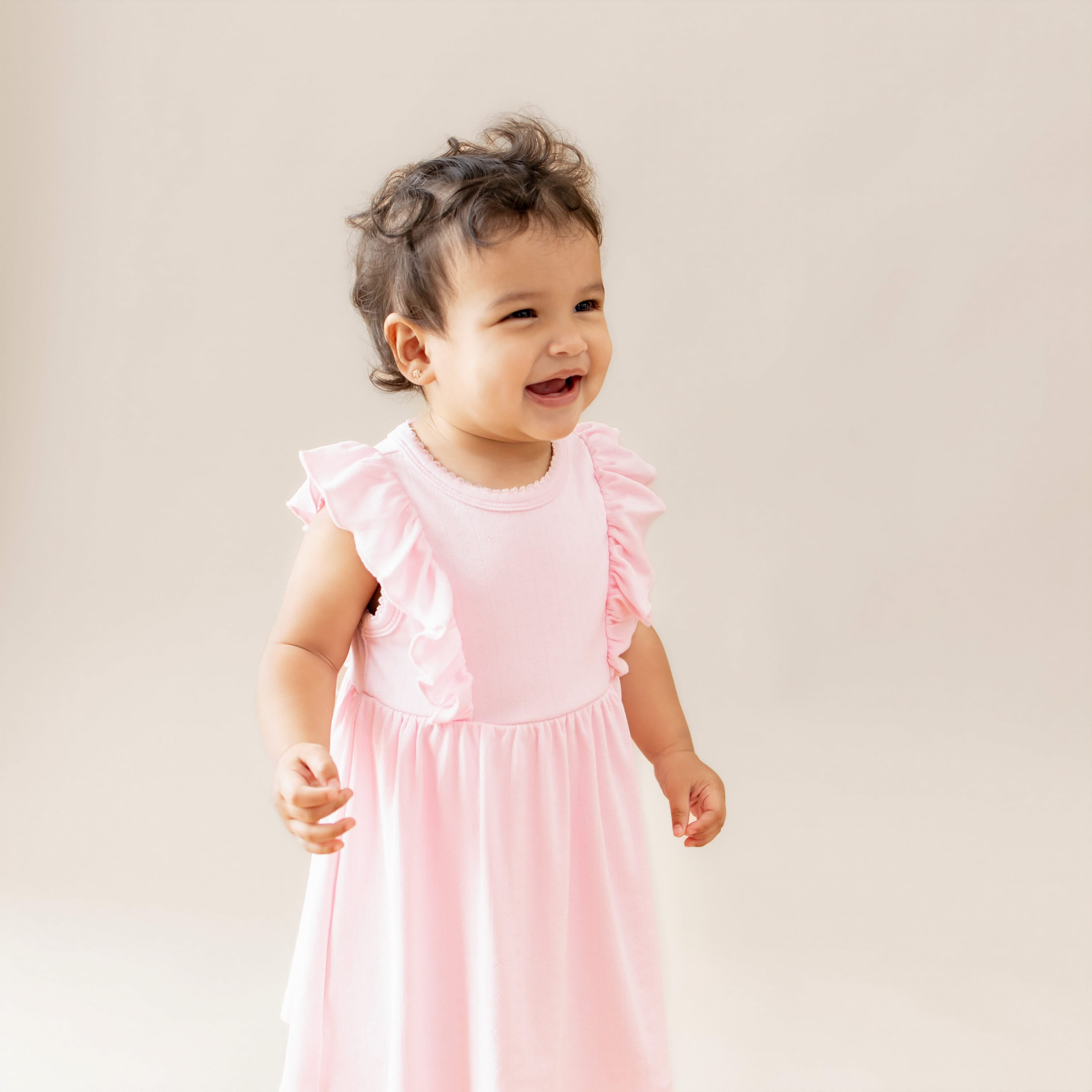 Child wearing a pink dress with ruffled sleeves against a plain background