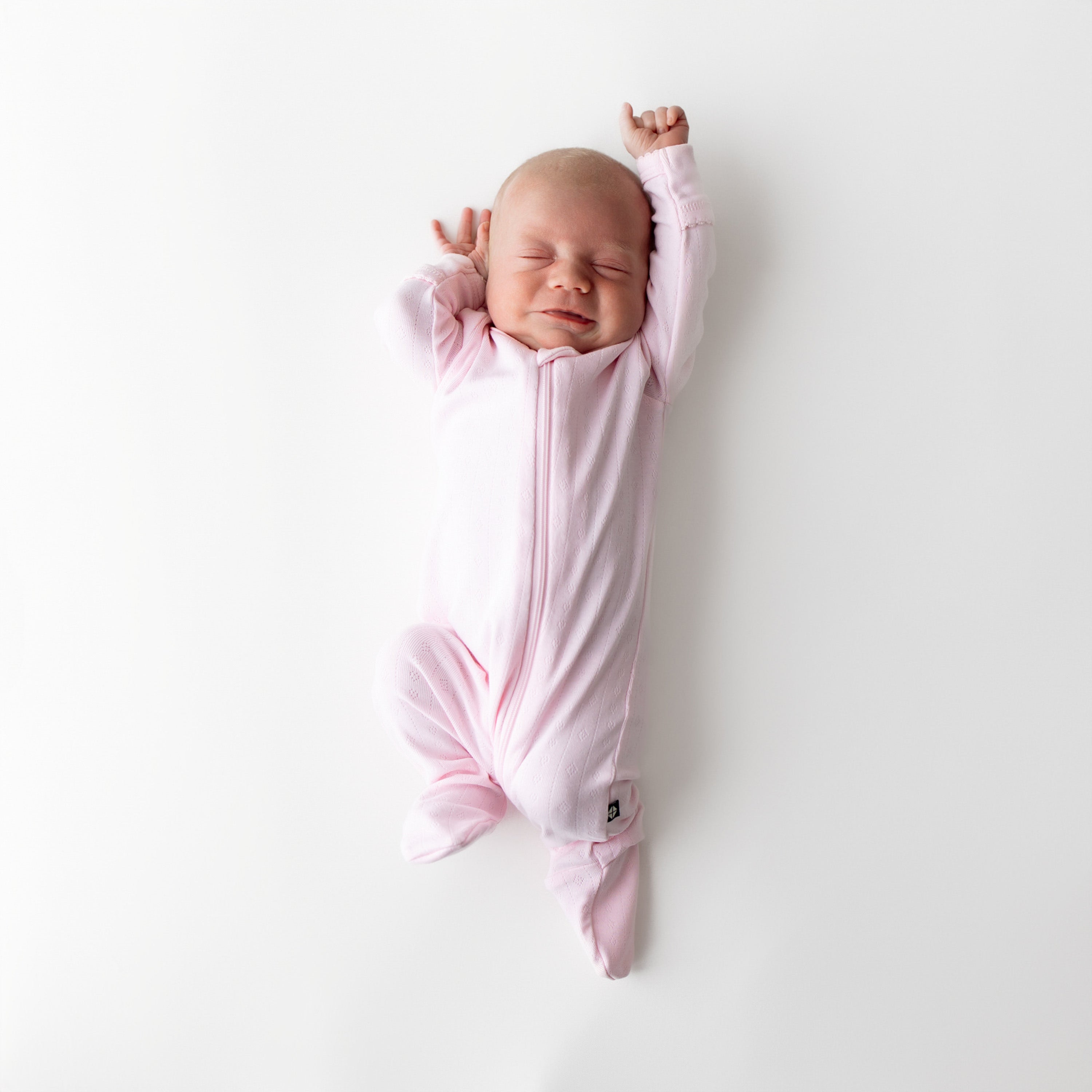 Newborn stretching wearing the Pointelle Zippered Footie in Sakura