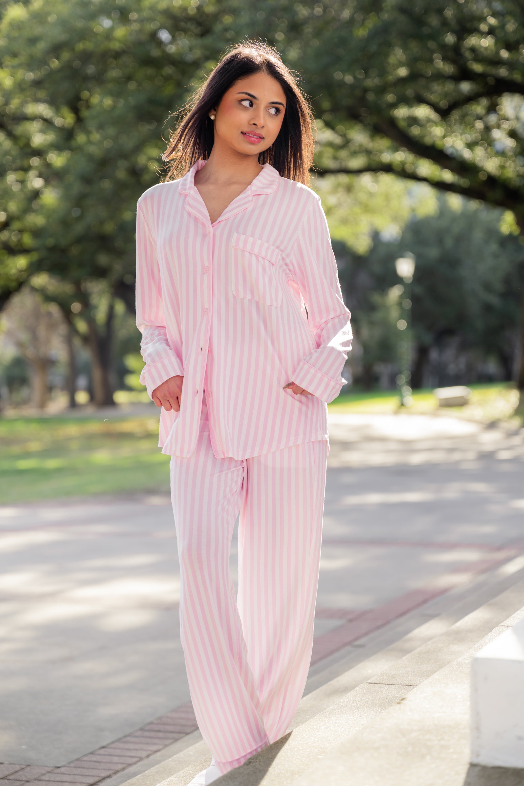 Woman wearing pink striped pajamas standing outdoors on a path with trees in the background