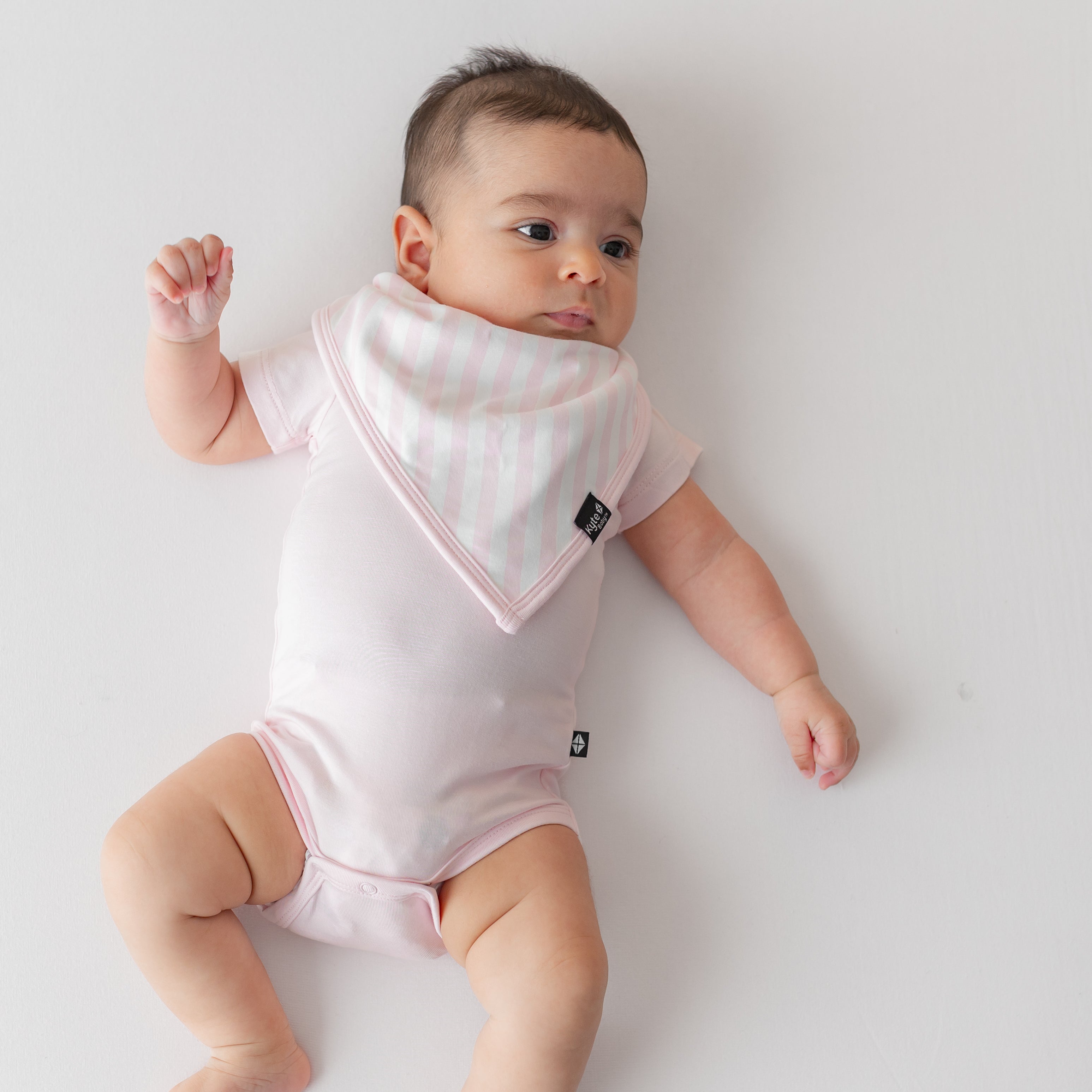 Young infant laying on a pink blanket wearing the absorbent Bib in Small Sakura Stripe paired with a short sleeve bodysuit in Sakura