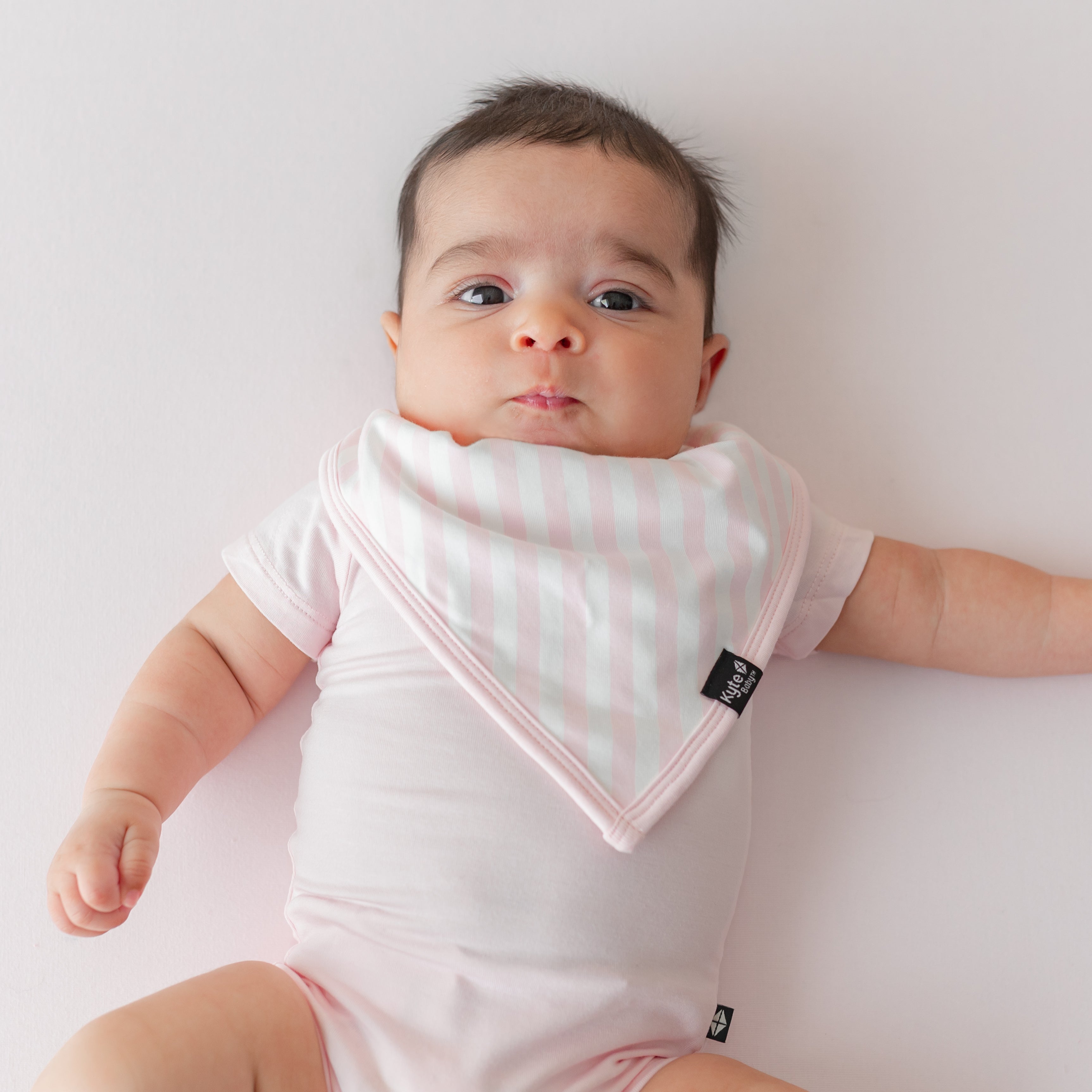 Close up of infant wearing the Bib in Small Sakura Stripe wearing a Sakura pink short sleeve bodysuit laying on a pink blanket