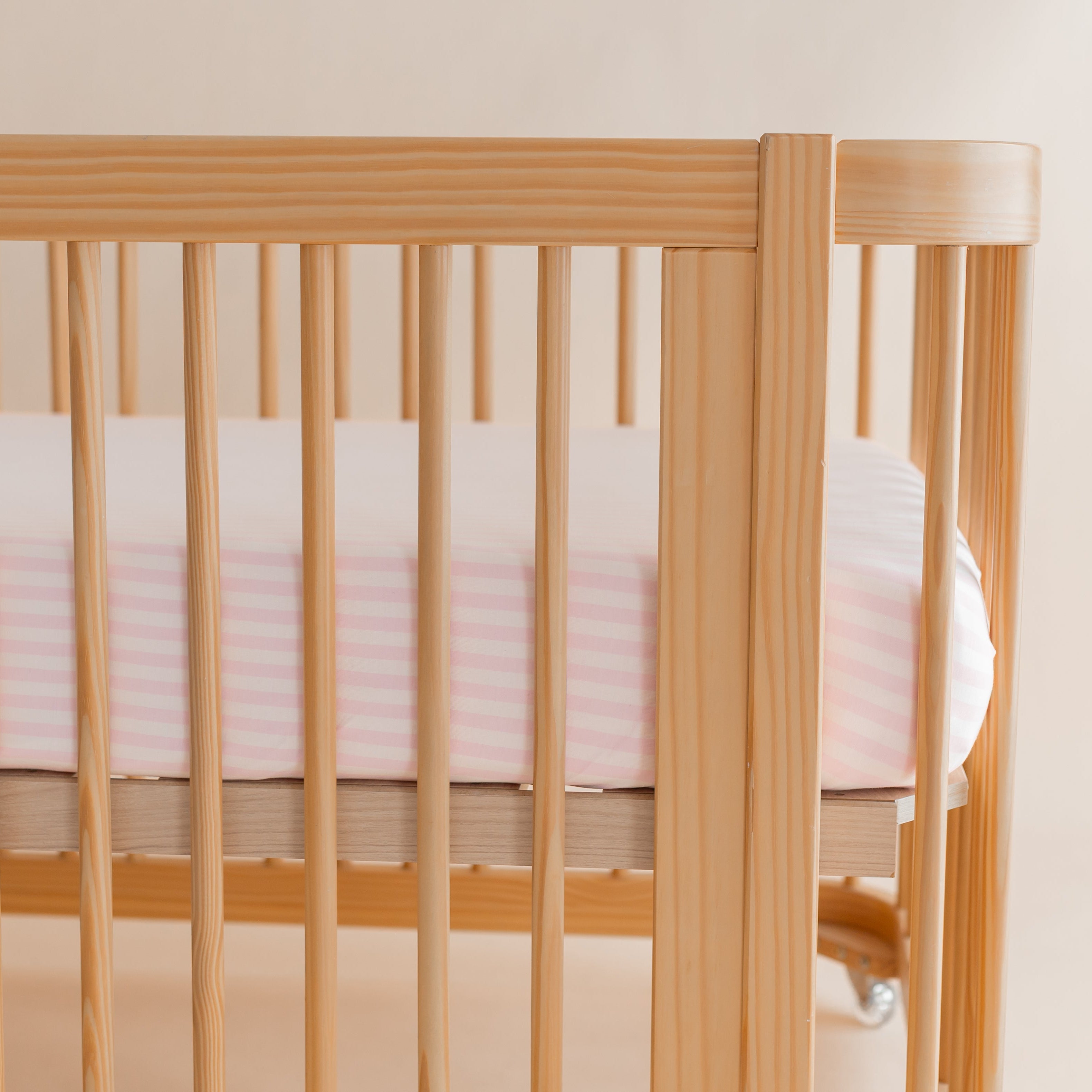 Soft and stretchy Crib Sheet in Small Sakura Stripe shown in a wooden crib