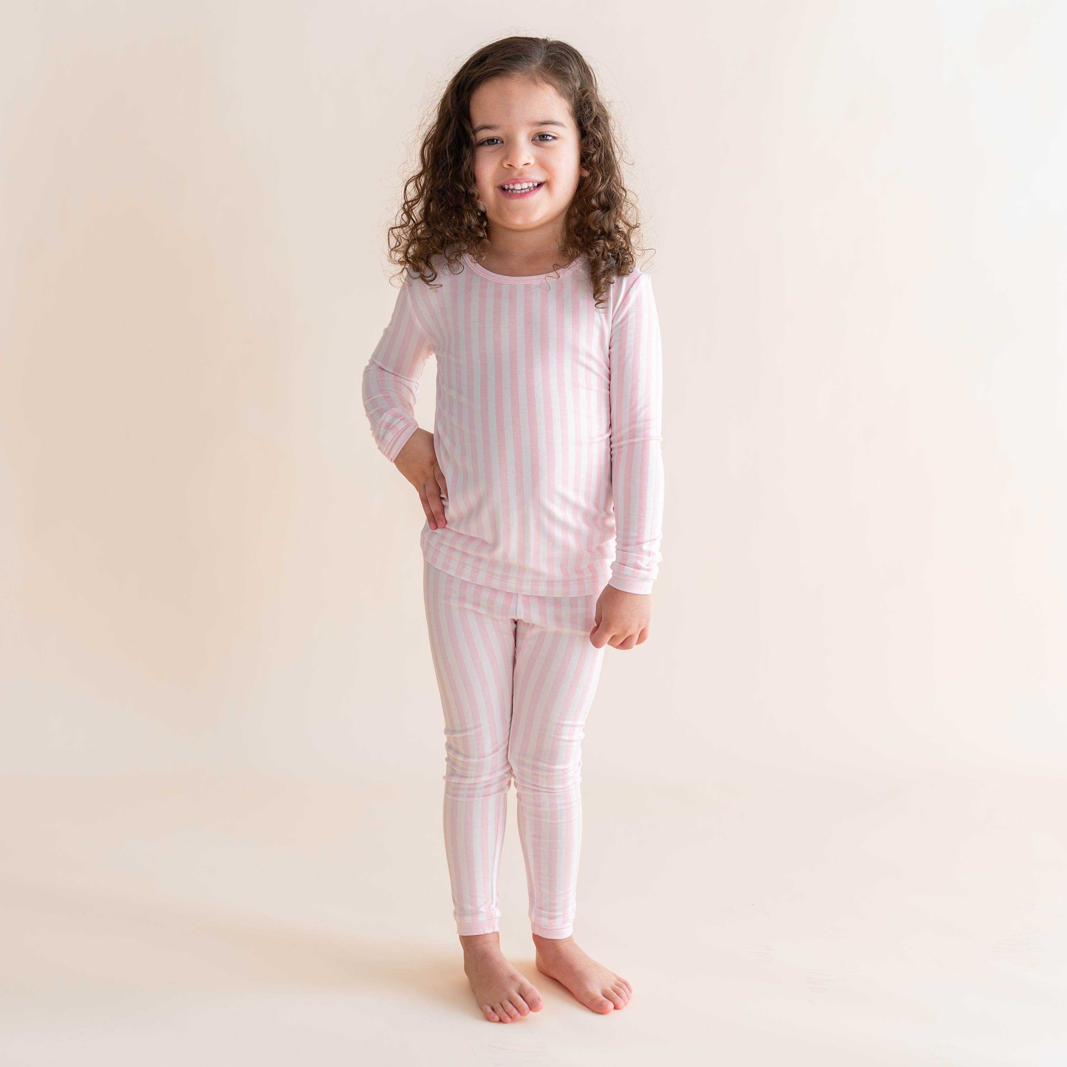 Young girl standing in front of a light cream background wearing the Long Sleeve Pajamas in Small Sakura Stripe