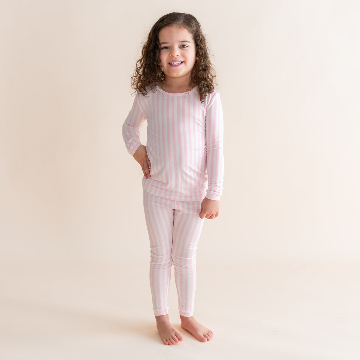 Young girl standing in front of a light cream background wearing the Long Sleeve Pajamas in Small Sakura Stripe