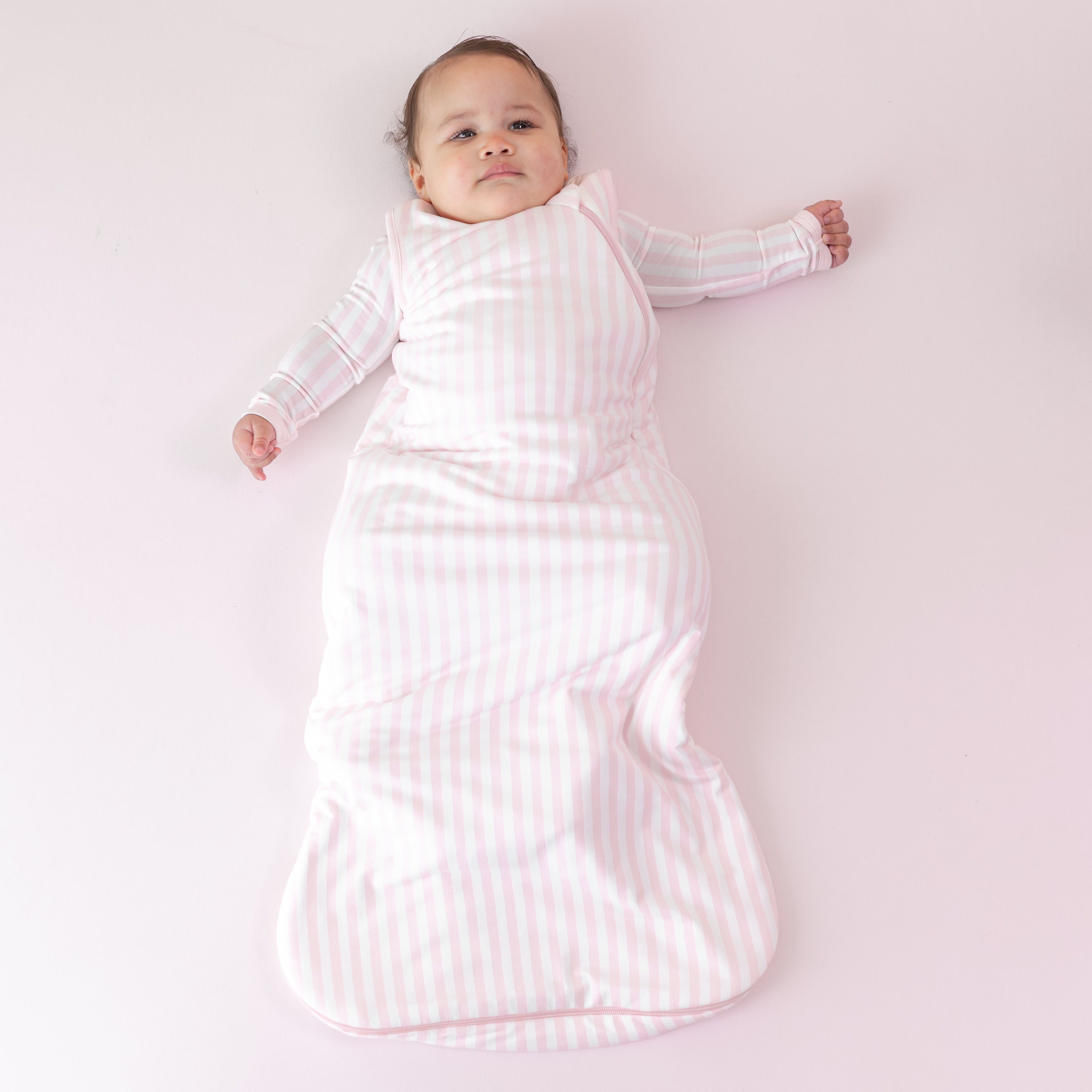 Infant laying on a pink blanket wearing the soft and breathable Sleep Bag in Small Sakura Stripe 1.0 and matching romper