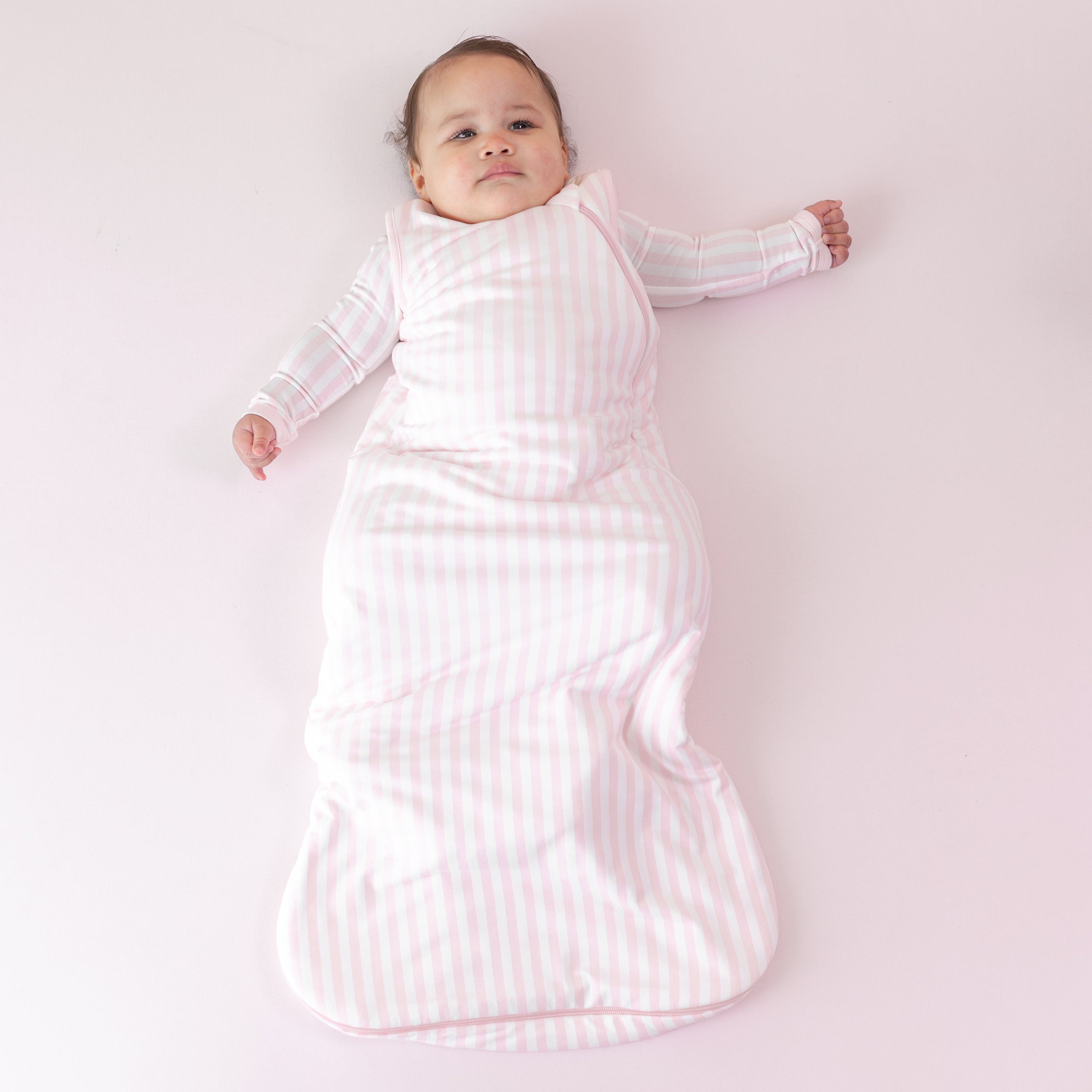 Infant laying on a pink blanket wearing the soft and breathable Sleep Bag in Small Sakura Stripe 1.0 and matching romper