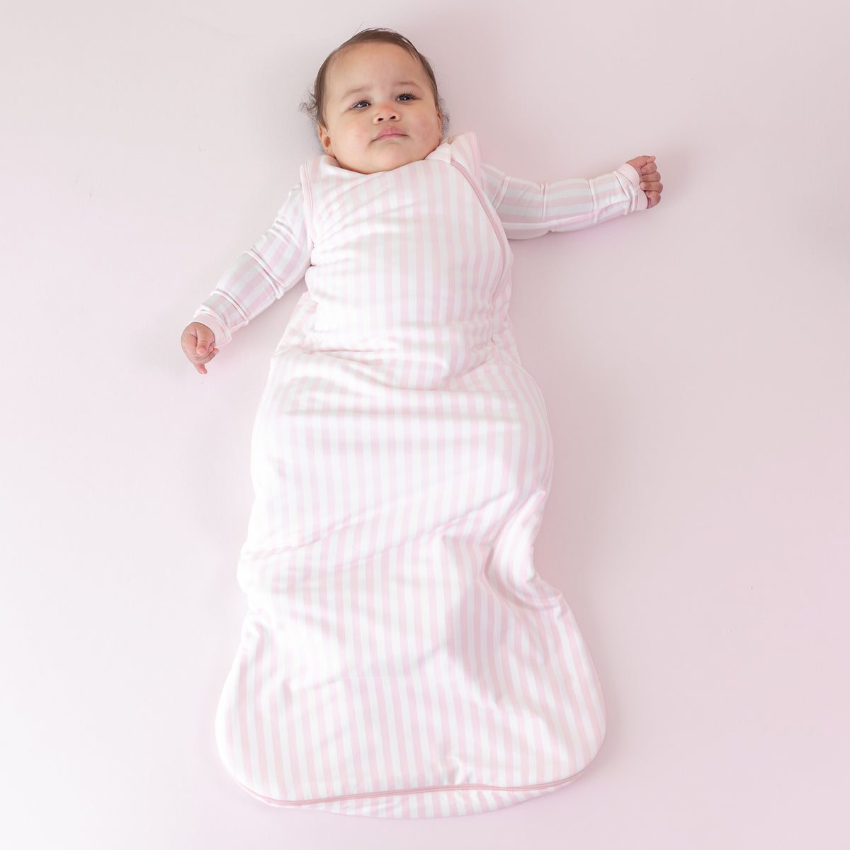 Infant laying on a pink blanket wearing the soft and breathable Sleep Bag in Small Sakura Stripe 1.0 and matching romper