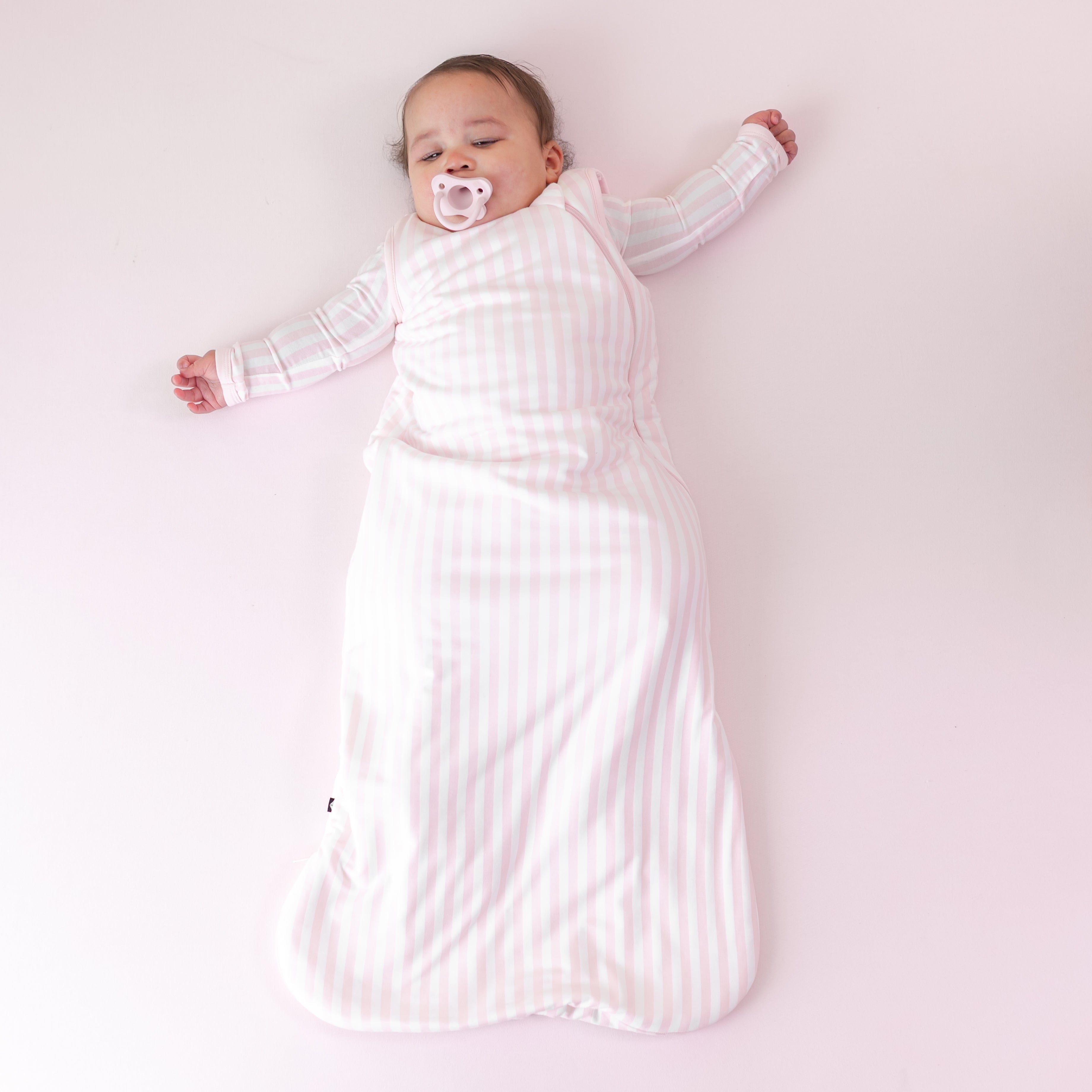 Sleeping infant laying on a pink blanket wearing the Sleep Bag in Small Sakura Stripe 1.0 and matching romper