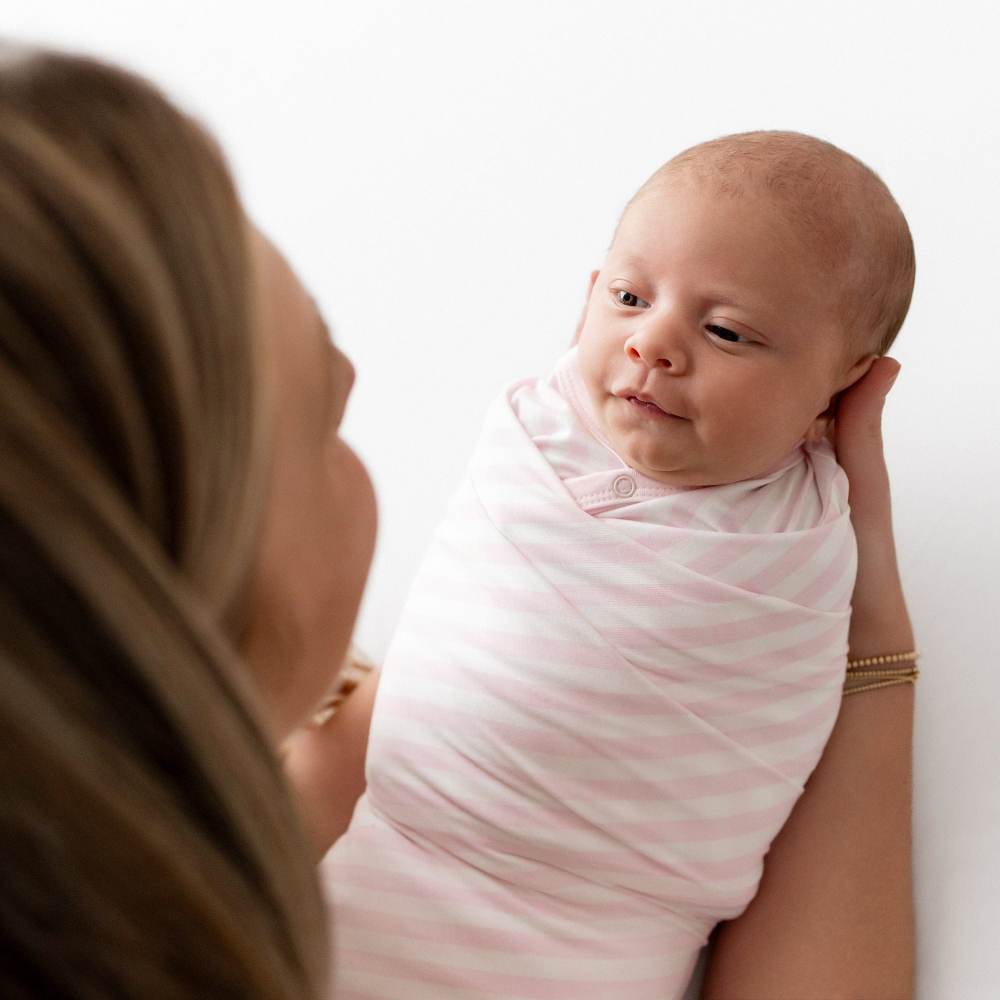 Newborn being held by her mother swaddled in the Swaddle Blanket in Small Sakura Stripe