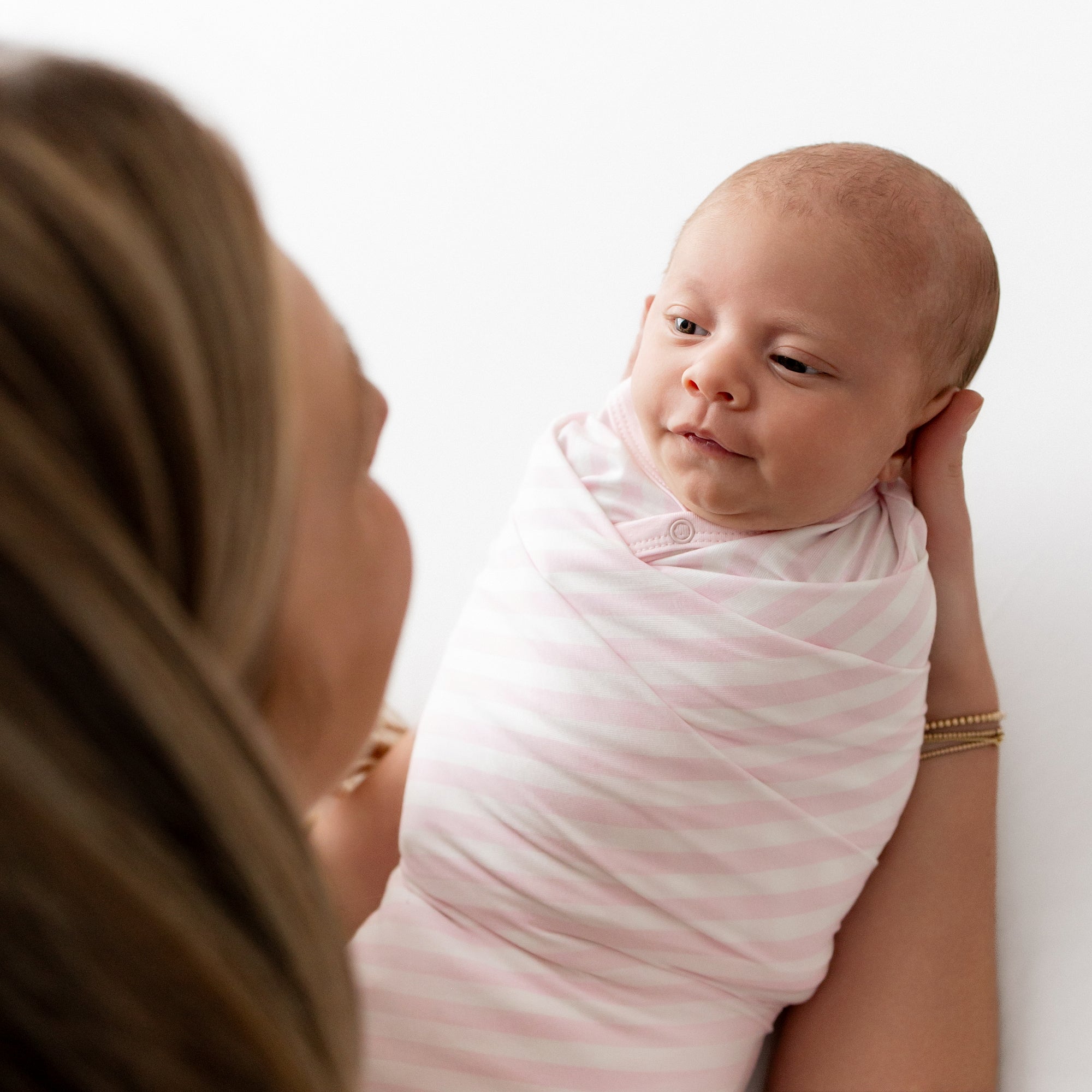 Newborn being held by her mother swaddled in the Swaddle Blanket in Small Sakura Stripe