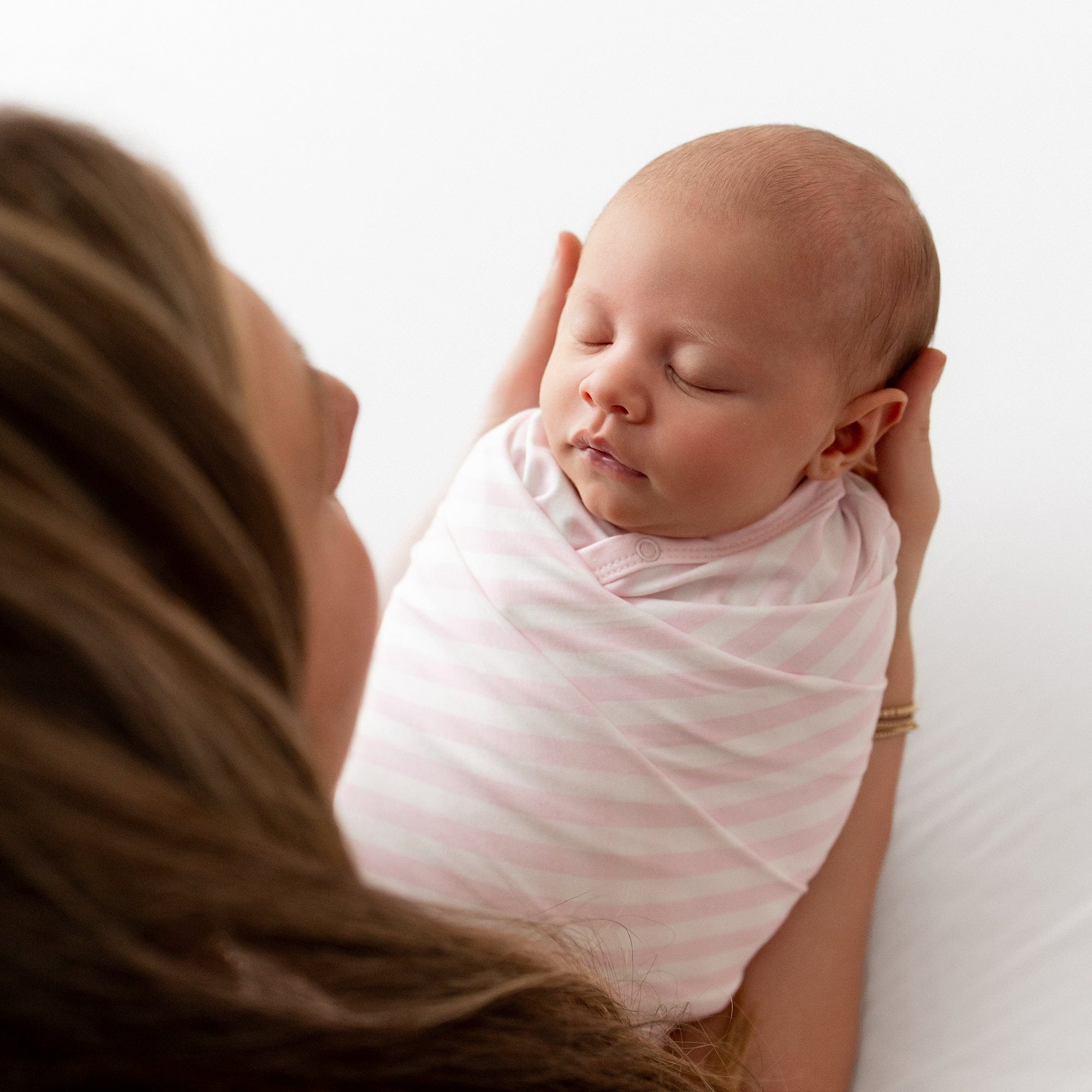 Sleeping newborn being held by her mother swaddled in the Swaddle Blanket in Small Sakura Stripe