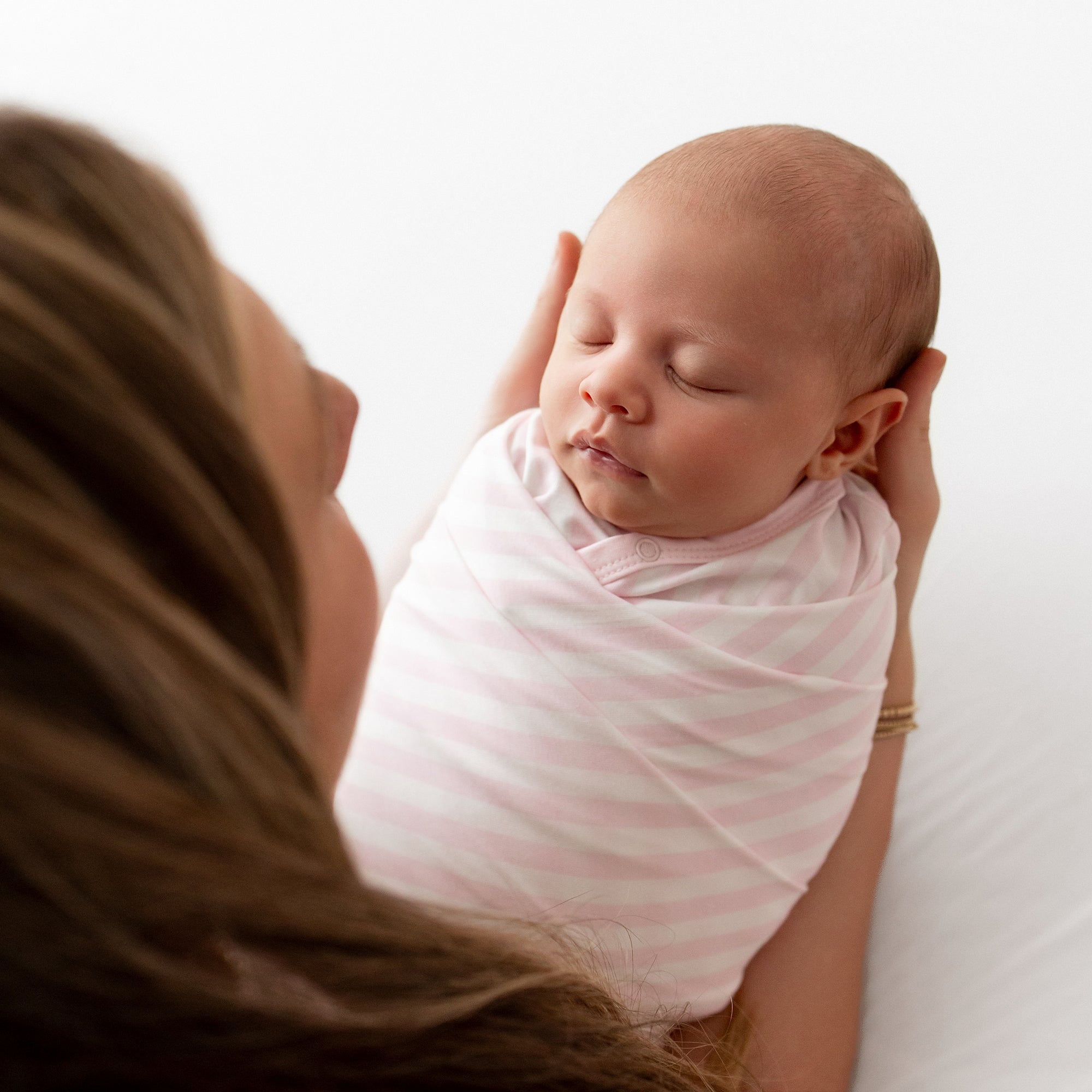 Sleeping newborn being held by her mother swaddled in the Swaddle Blanket in Small Sakura Stripe