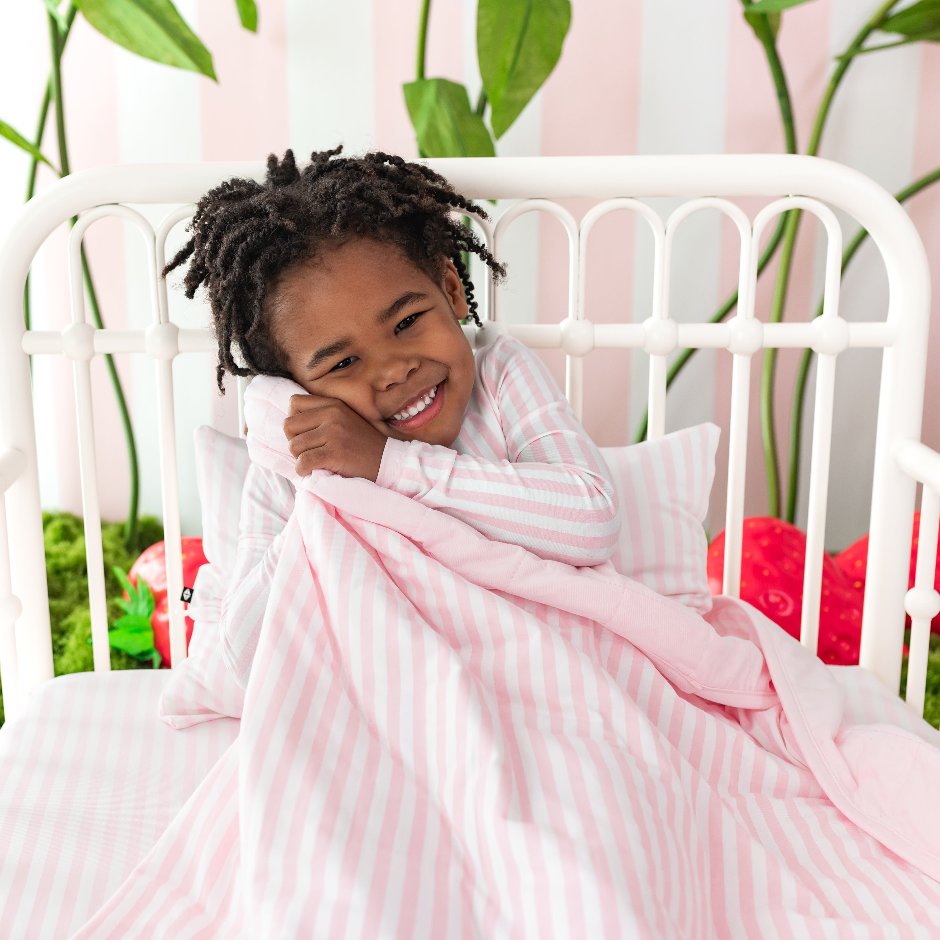 Young girl laying in bed with the toddler Blanket in Small Sakura Stripe 1.0 over top of her