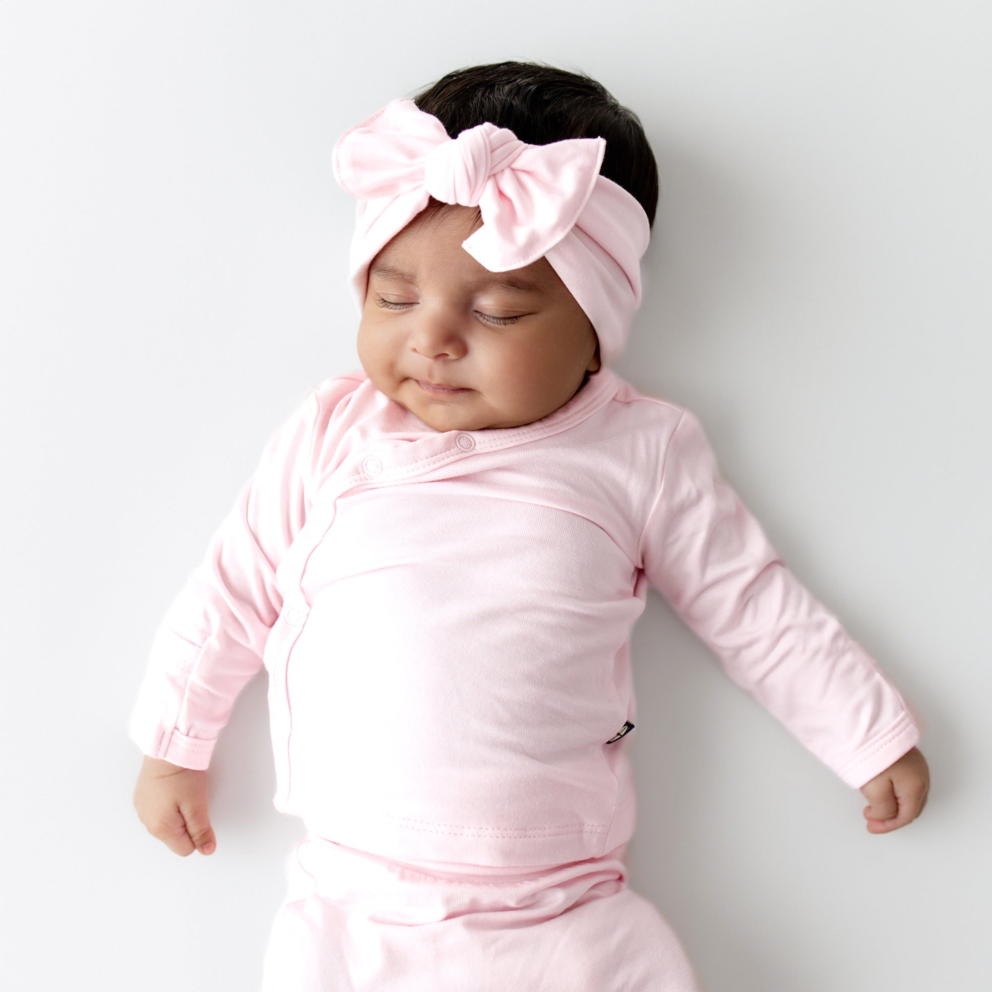 Baby in pink outfit with a large bow headband on a light gray background