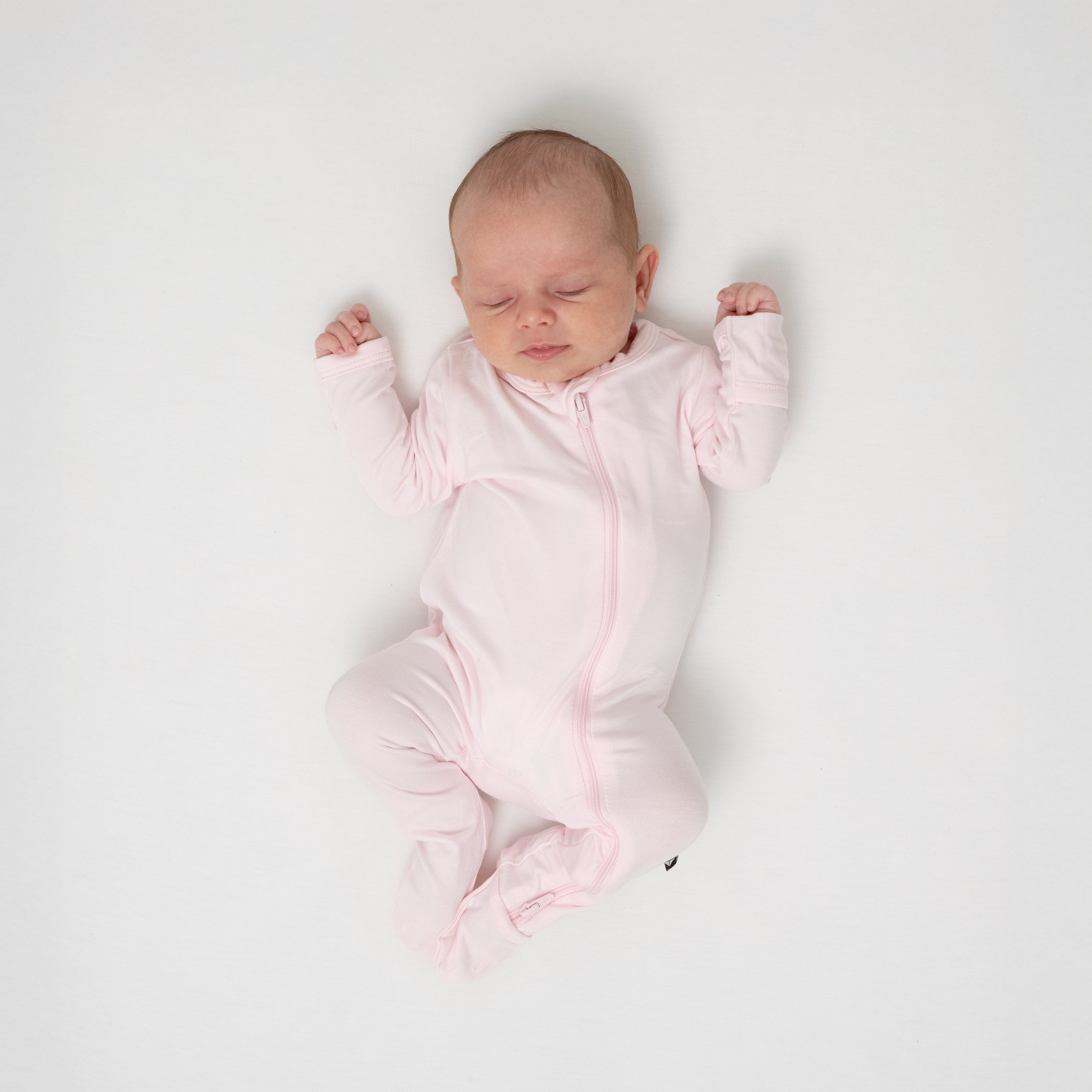 Sleeping infant wearing the Zippered Footie in Sakura with her arms up b her shoulders