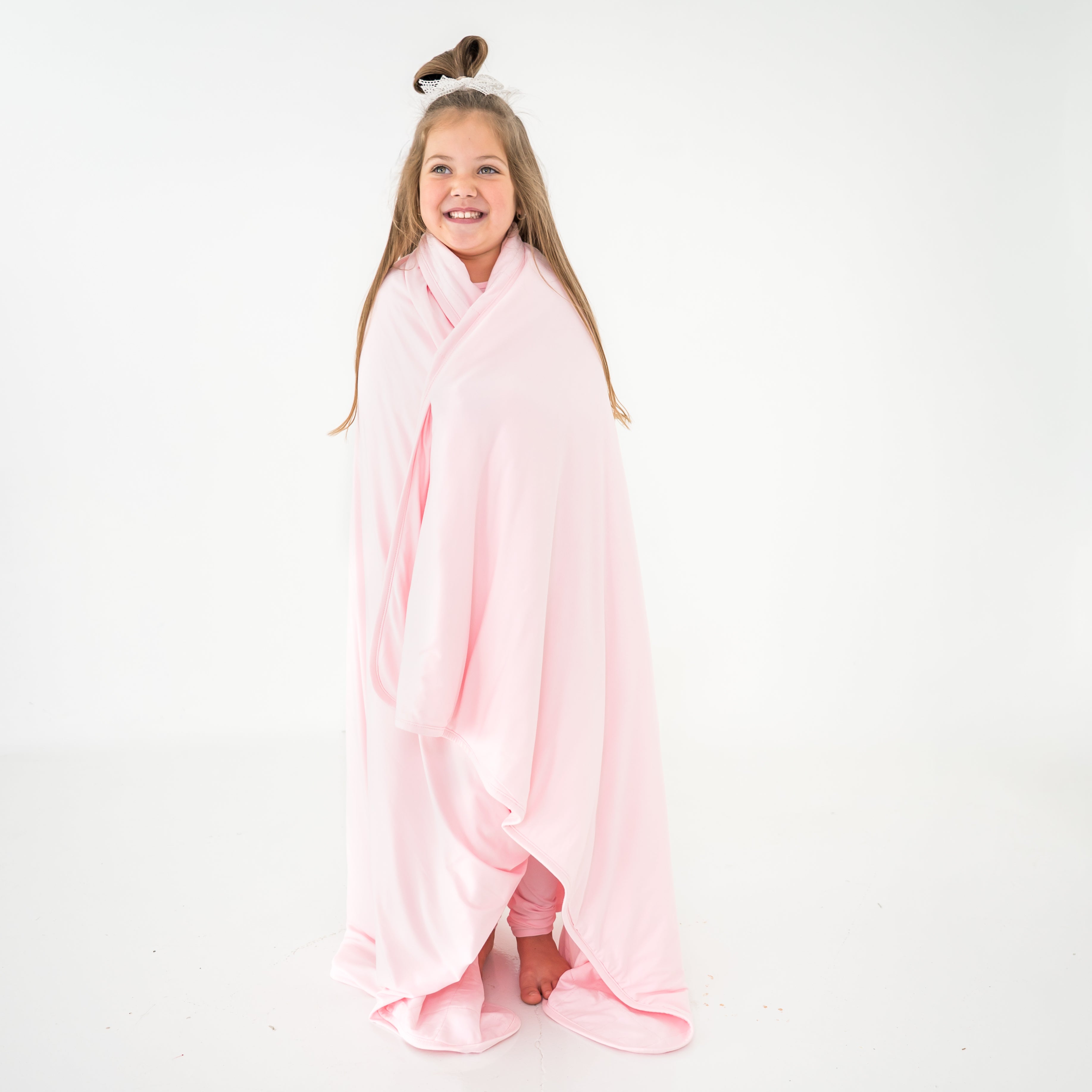 Young girl wrapped in a pink bamboo quilted blanket on a white background