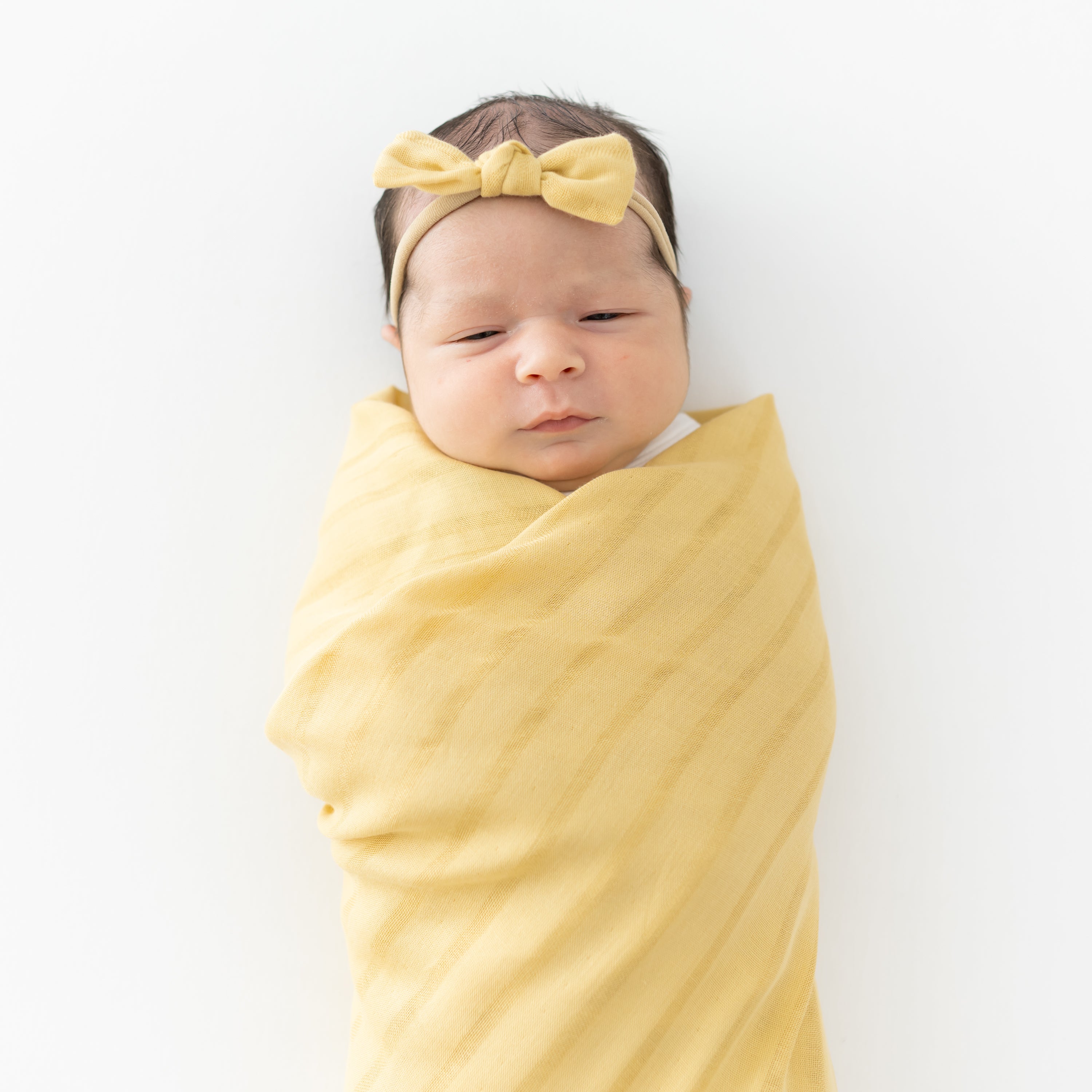 Newborn swaddled in blanket with matching Bamboo Muslin Tiny Bow in Sandcastle Yellow