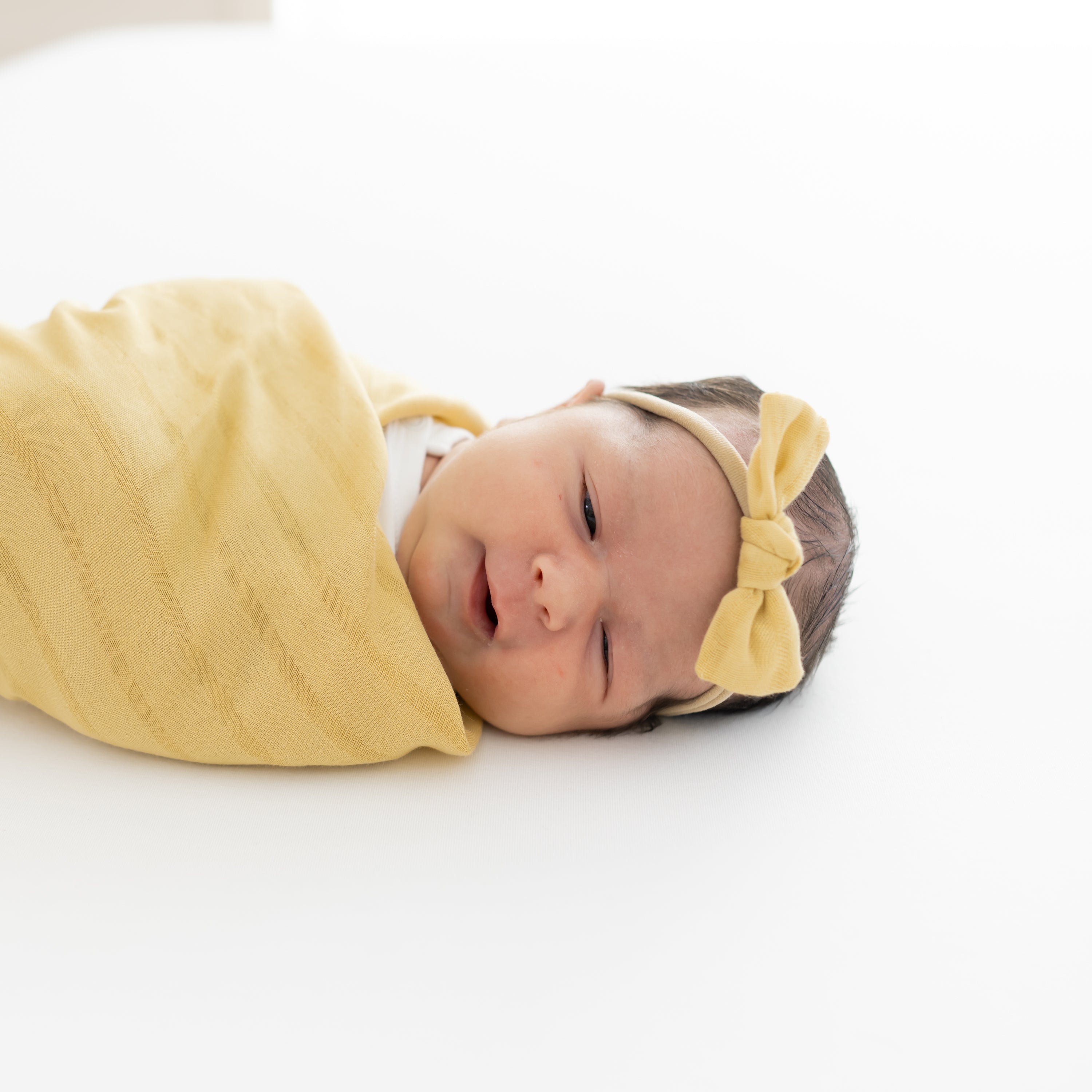 Newborn wearing Bamboo Muslin Tiny Bow in Sandcastle with matching yellow swaddle blanket