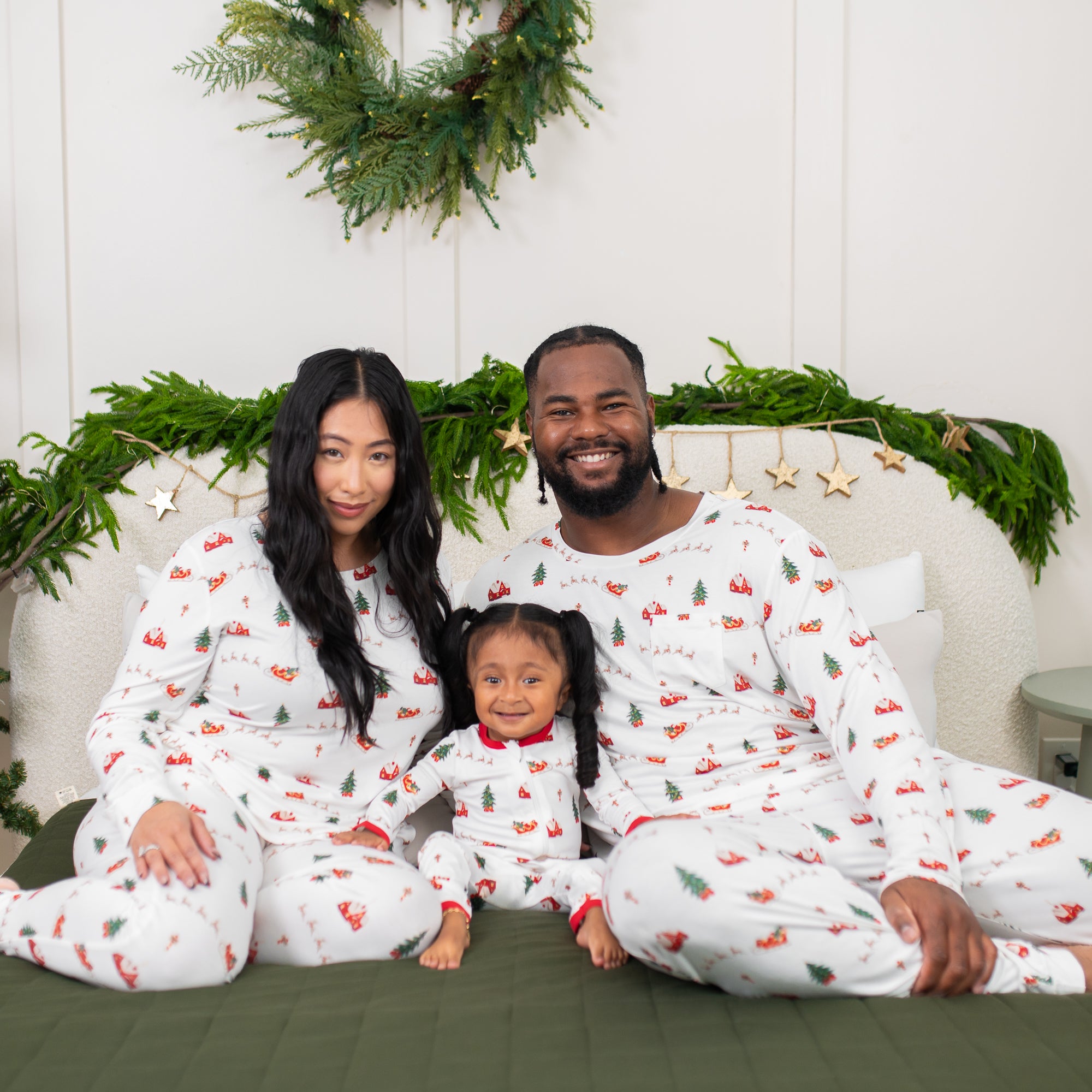 Family of 3 sitting on a bed matching in Santa Sleigh items