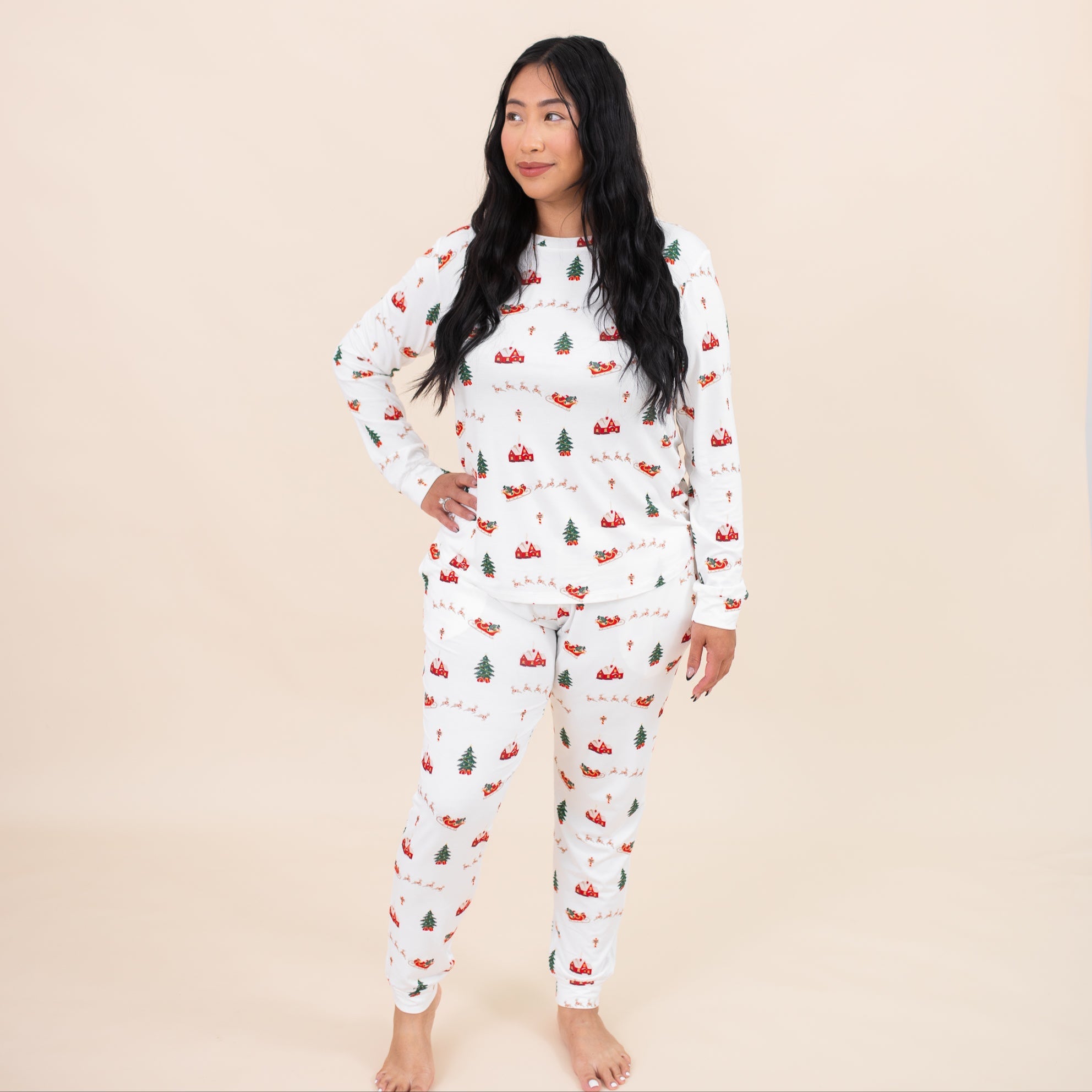 Female modeling the Women's Jogger Pajama Set in Santa Sleigh with one hand on hip in front of a light beige backdrop