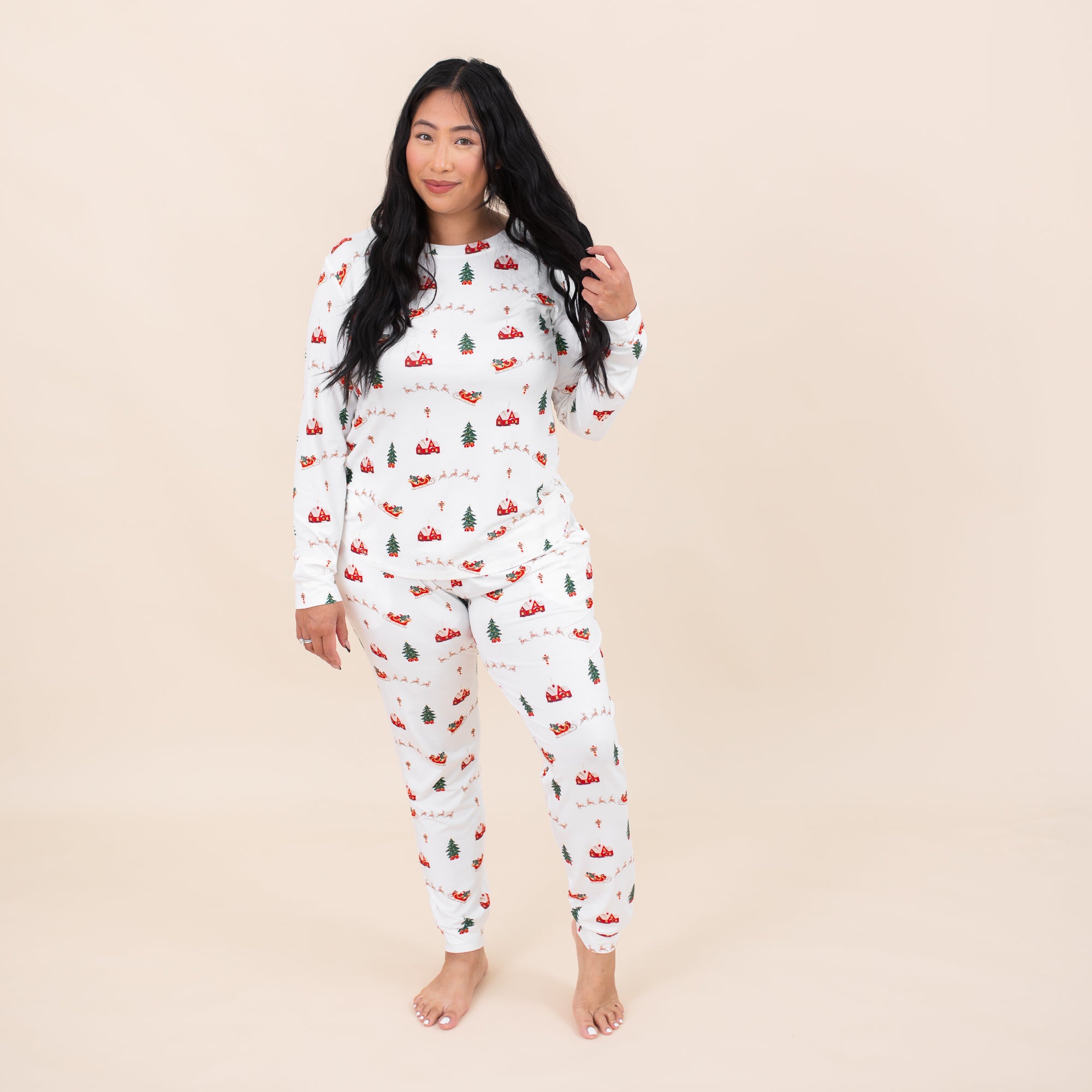 Female model standing in front of a light beige backdrop wearing the Women's Jogger Pajama Set in Santa Sleigh