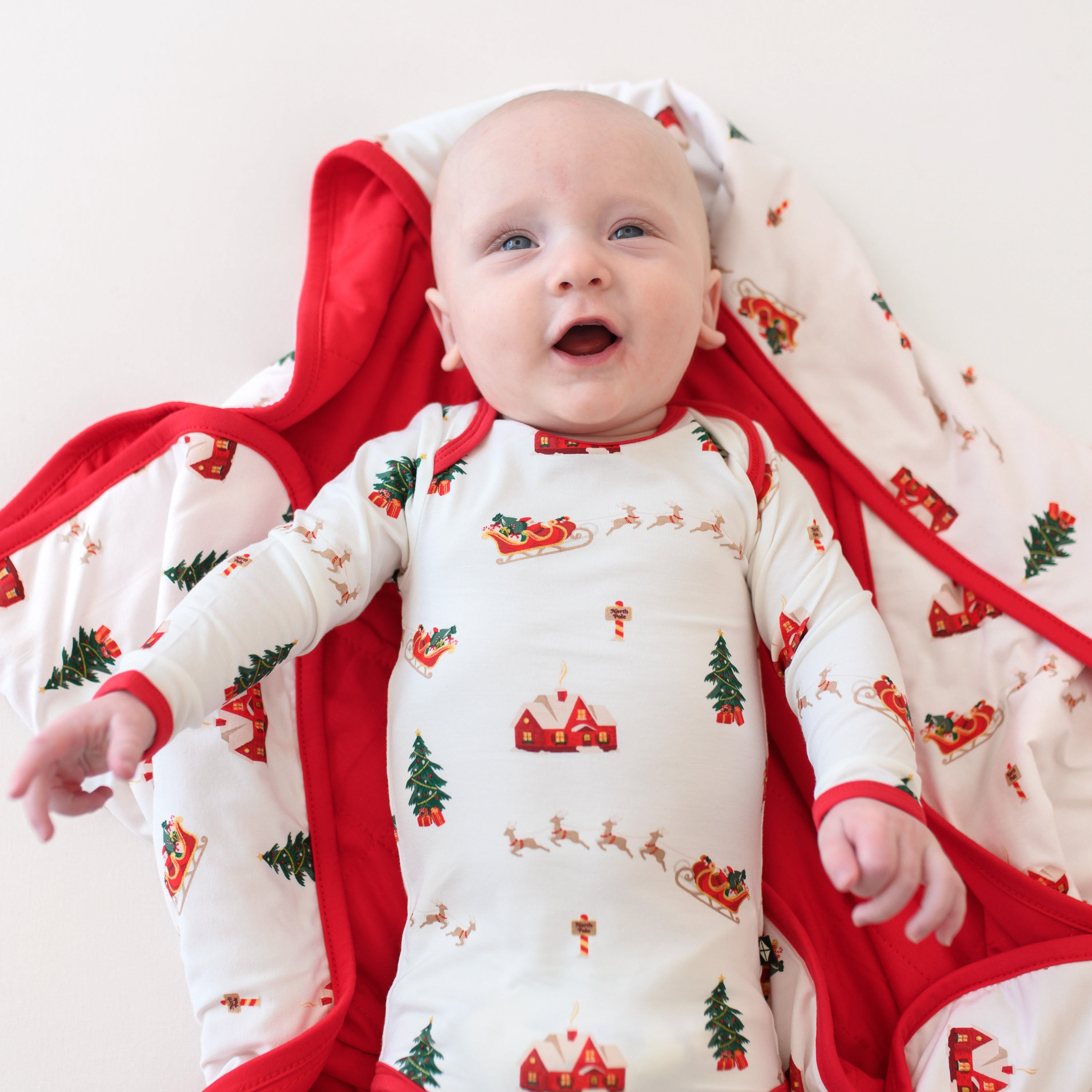 Close up of the Long Sleeve Bodysuit in Santa Sleigh shown on an infant laying on a matching blanket