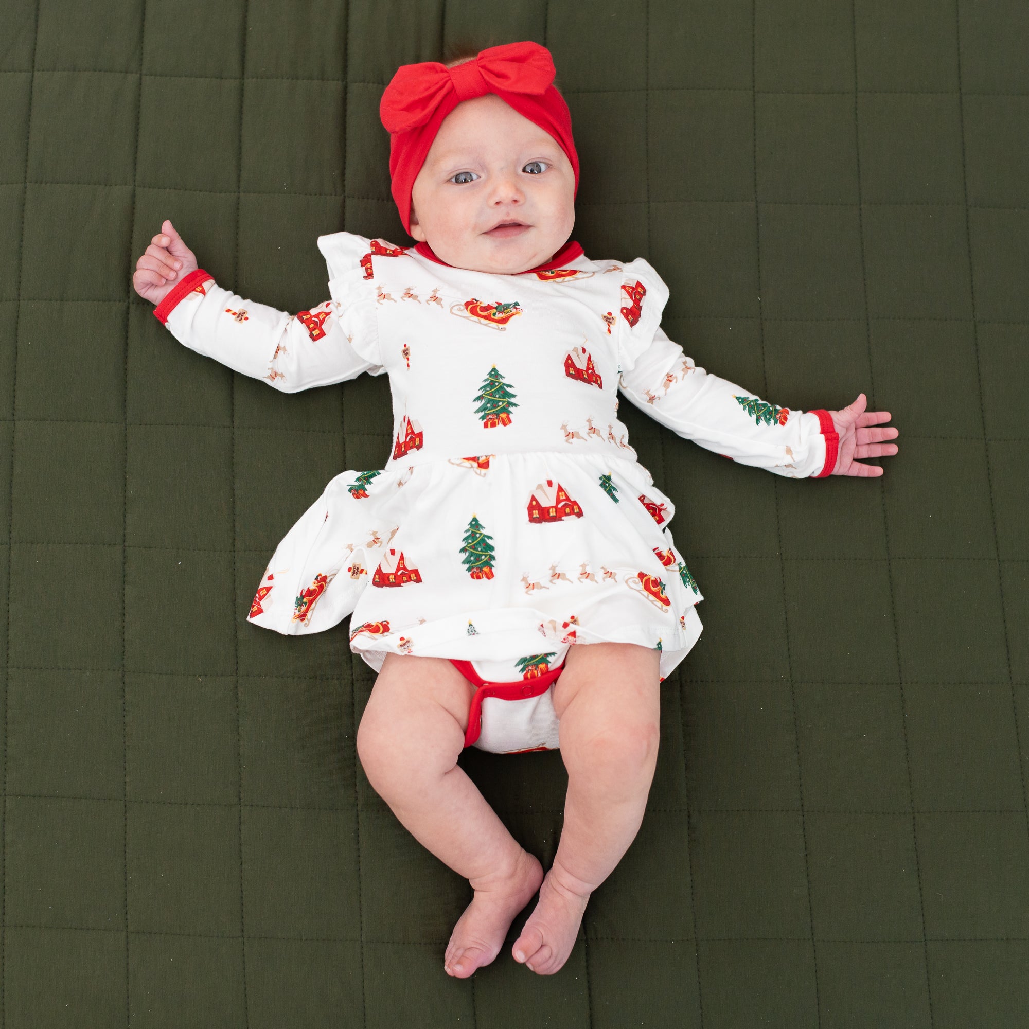 Infant laying down wearing the Bow Headband in Cardinal and Long sleeve twirl bodysuit dress in Santa Sleigh