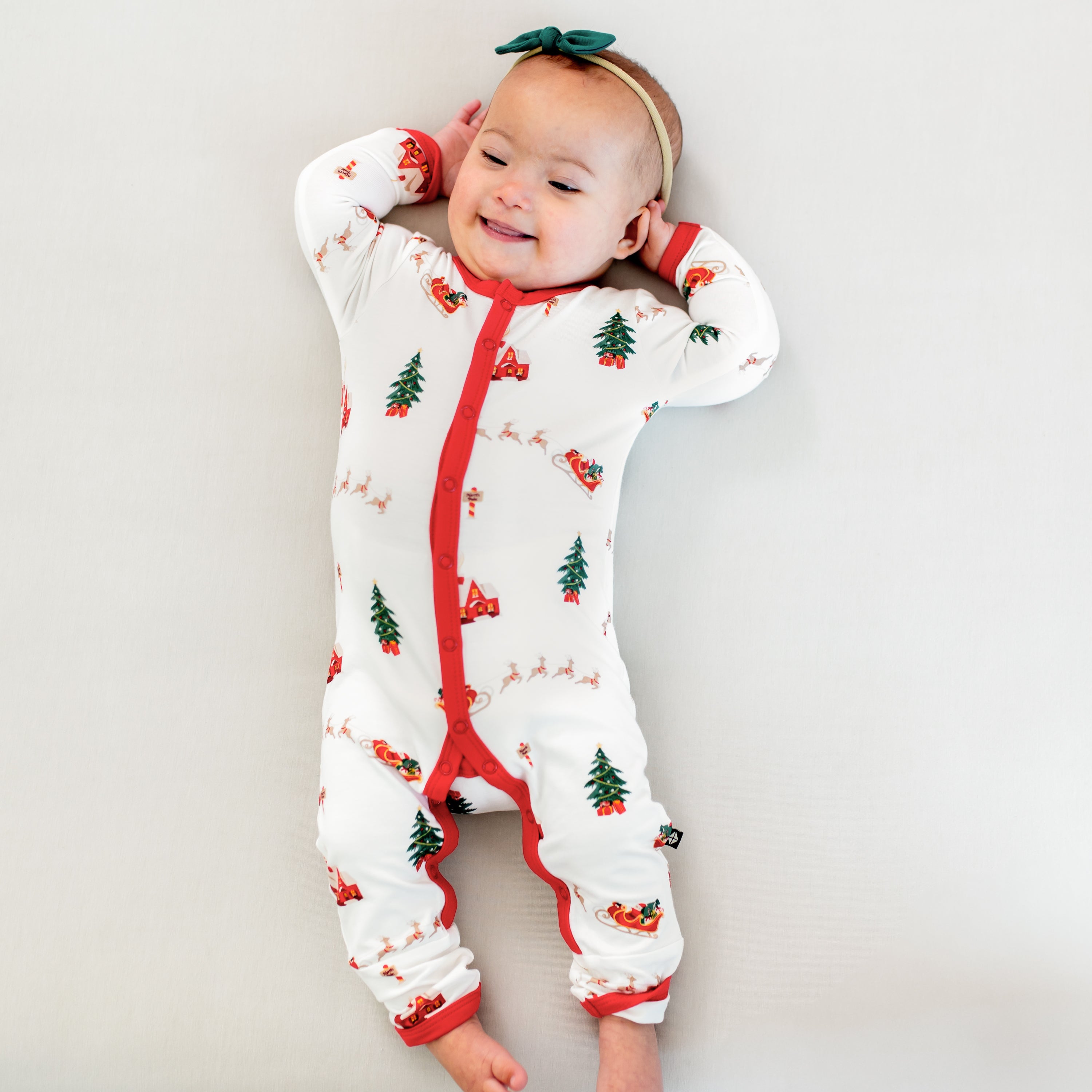 Smiling infant laying down wearing the Romper in Santa Sleigh with a Tiny Nylon bow in emerald