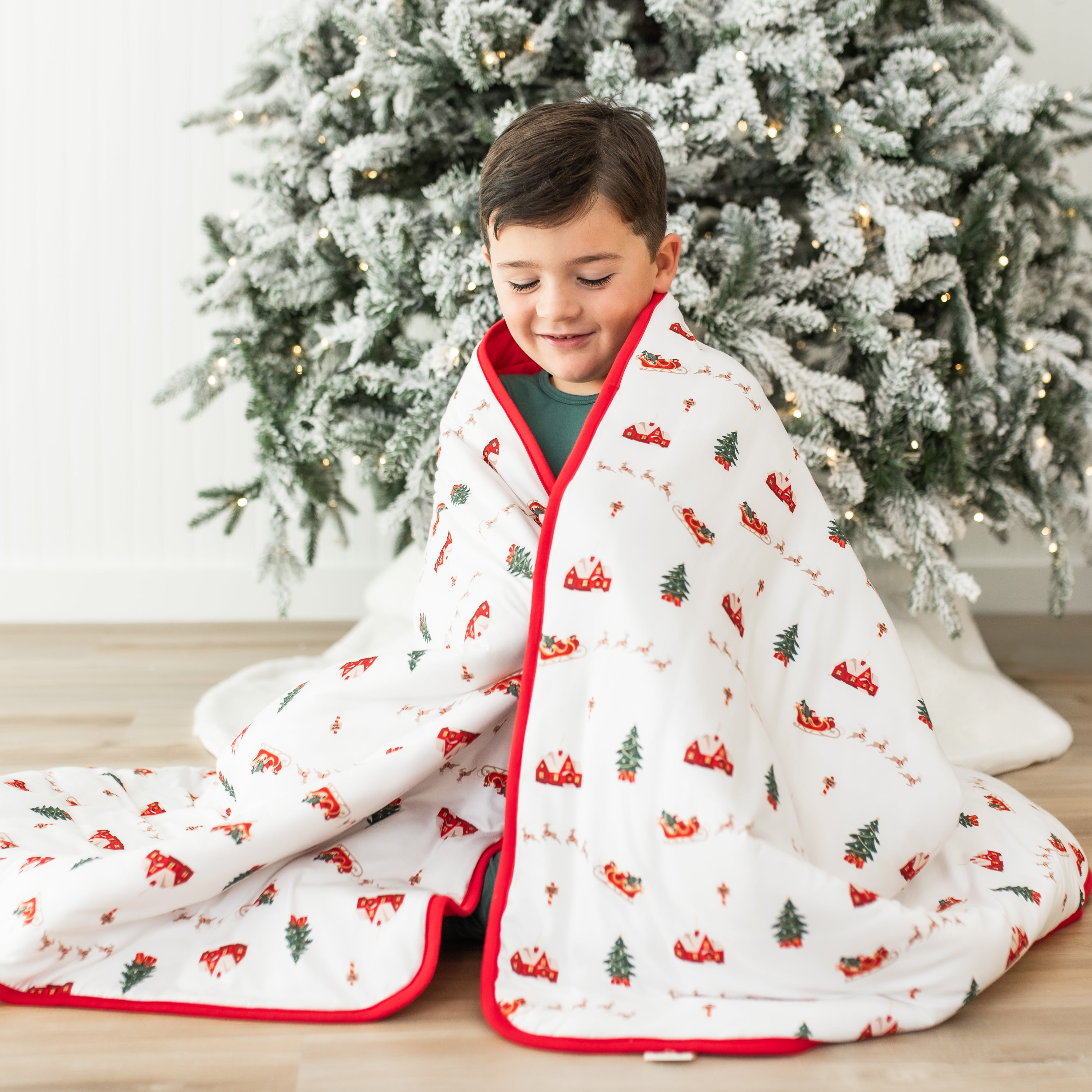 Young boy sitting on the floor with the Youth Blanket in Santa Sleigh 2.5 over his shoulders