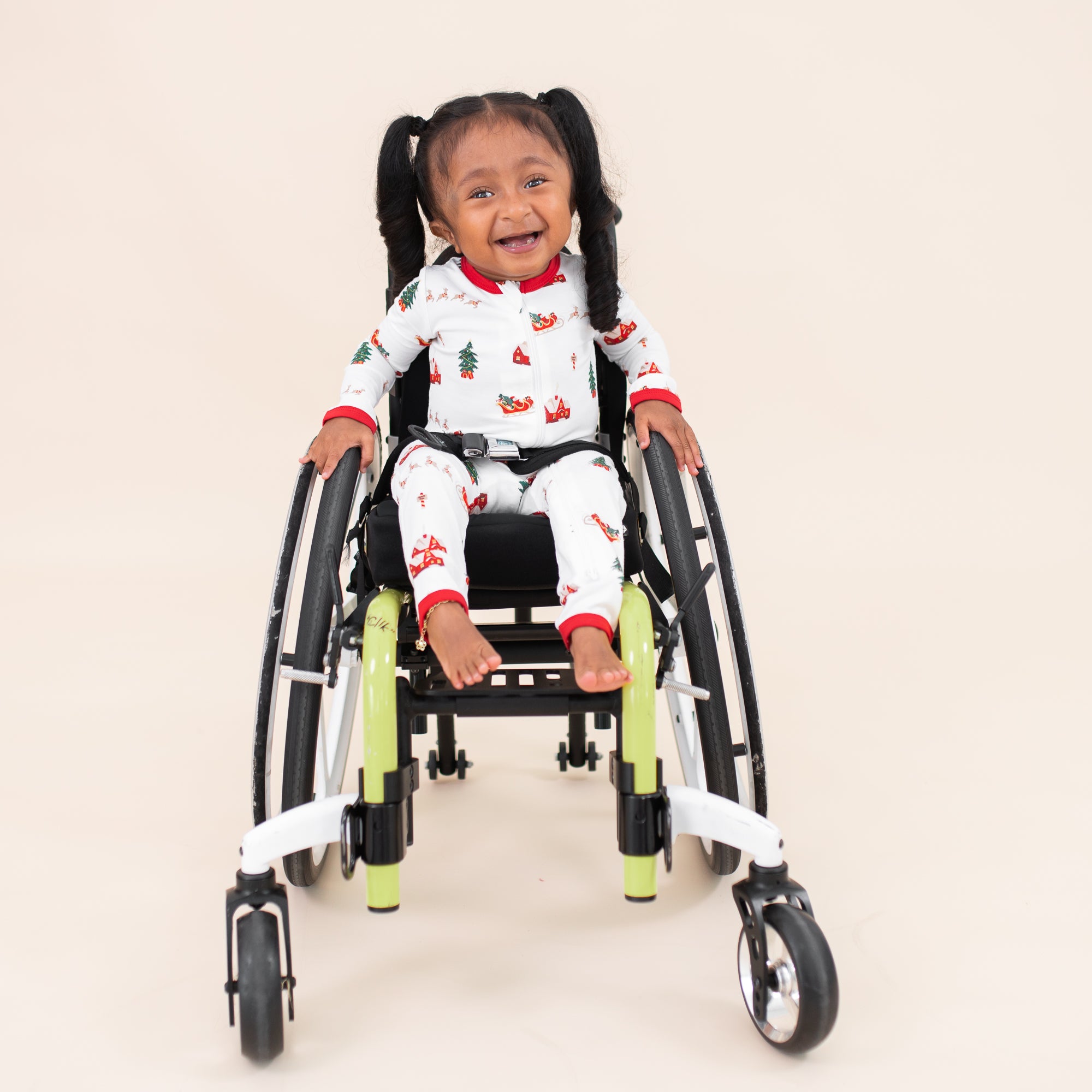 Young girl sitting in her wheelchair wearing the Zippered Romper in Santa Sleigh