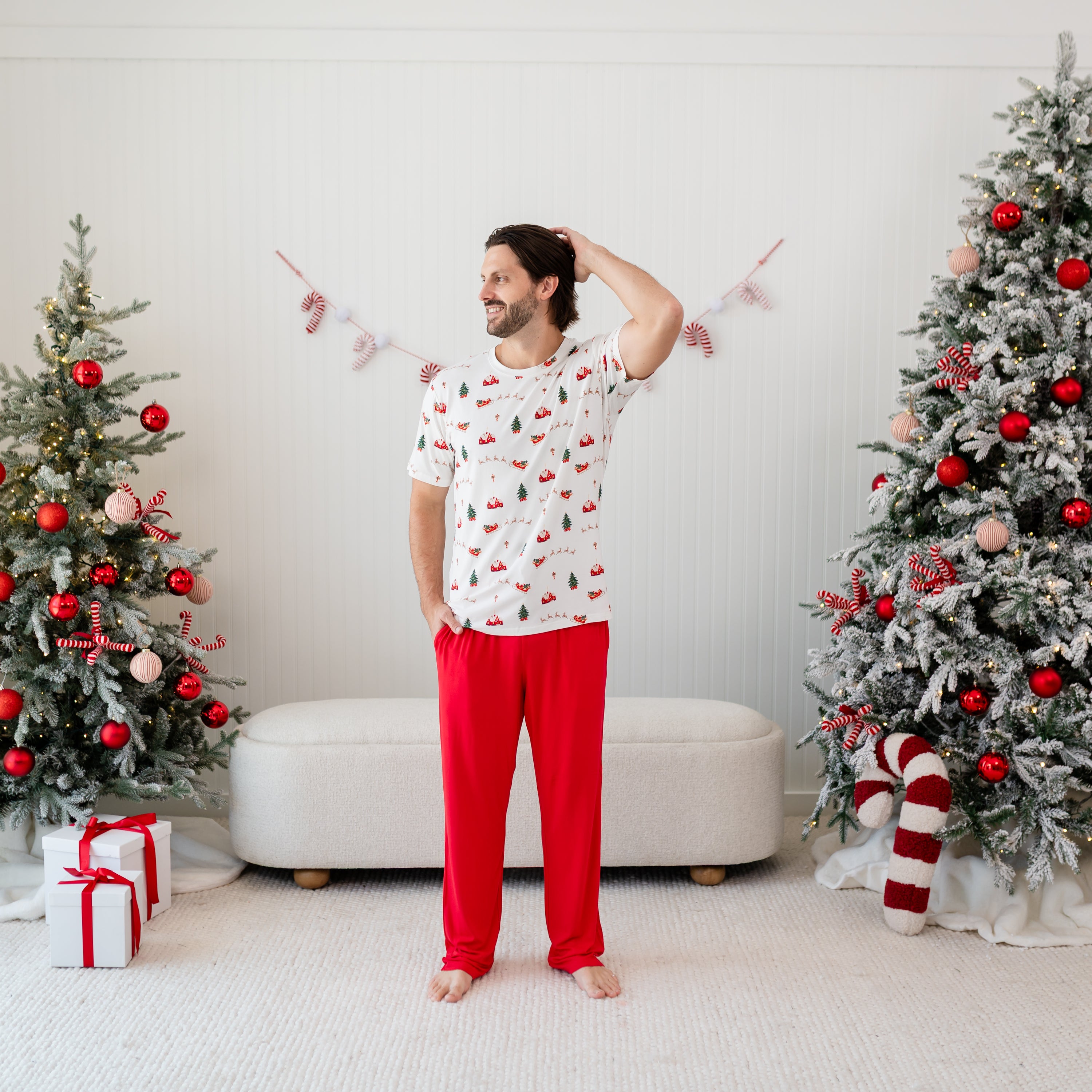 Male model standing in front of Christmas decor wearing the Men's Lounge Pants in Cardinal and Santa Sleigh Men's Crew Neck Tee